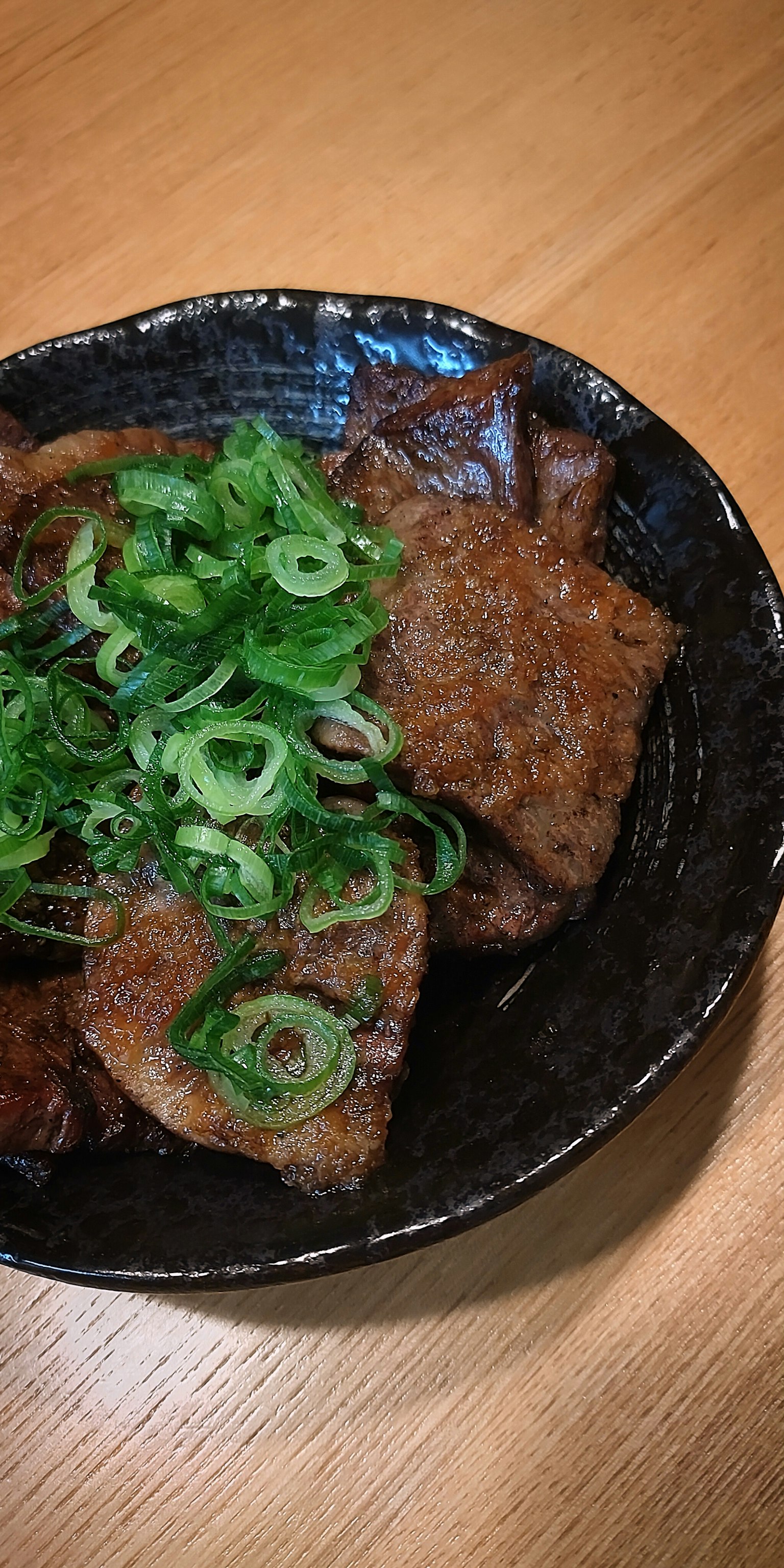 Piatto di carne guarnito con cipolle verdi in una ciotola nera