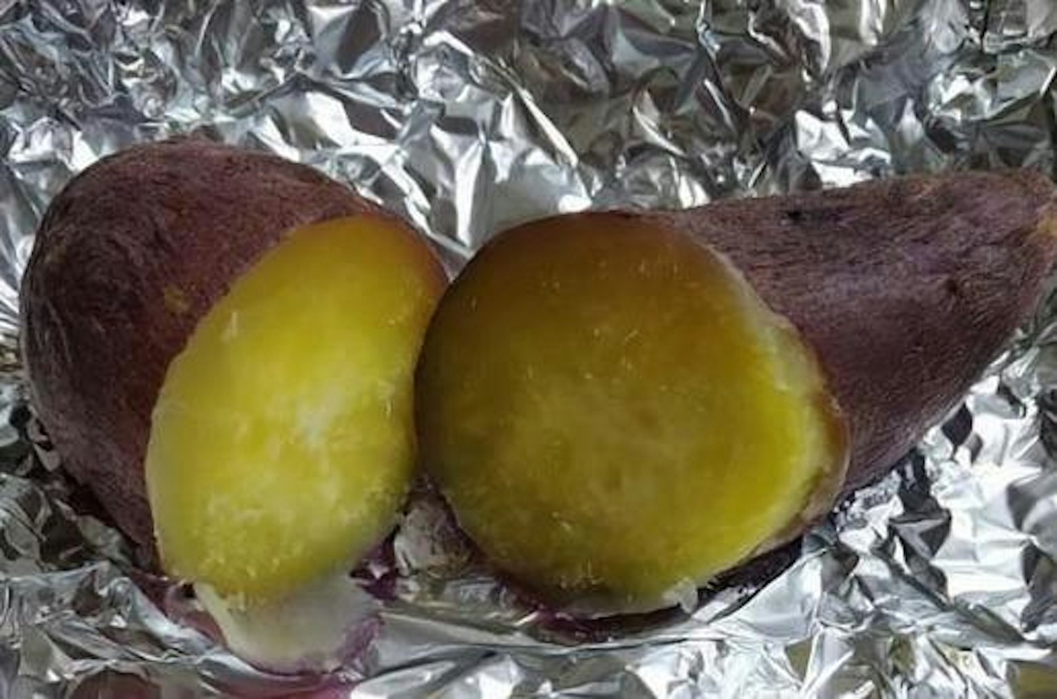 Une patate douce violette coupée en deux sur du papier aluminium argenté