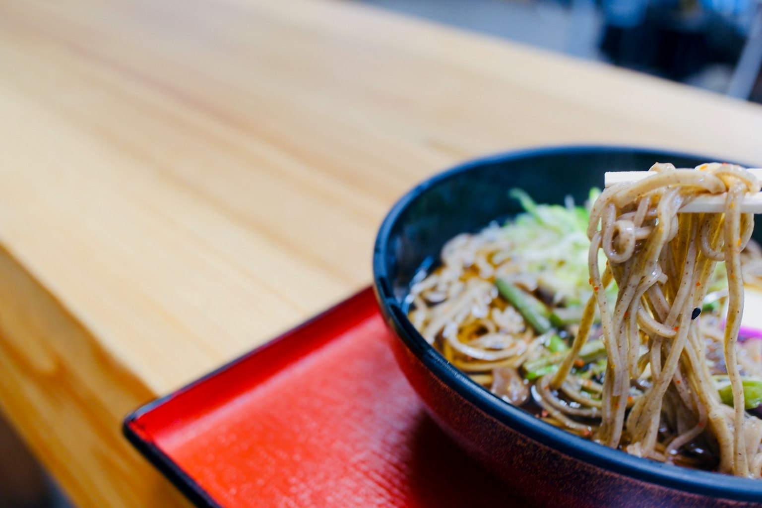 Schüssel mit Soba-Nudeln und Gemüse auf einem Holztisch