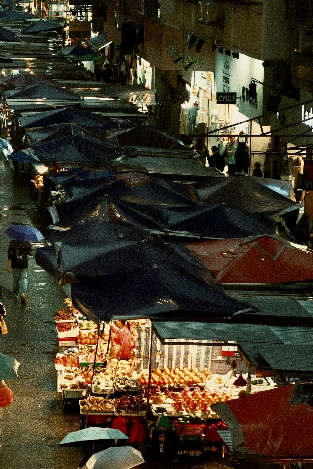 屋台の並ぶ路地と折りたたみ傘のある夜の市場通り