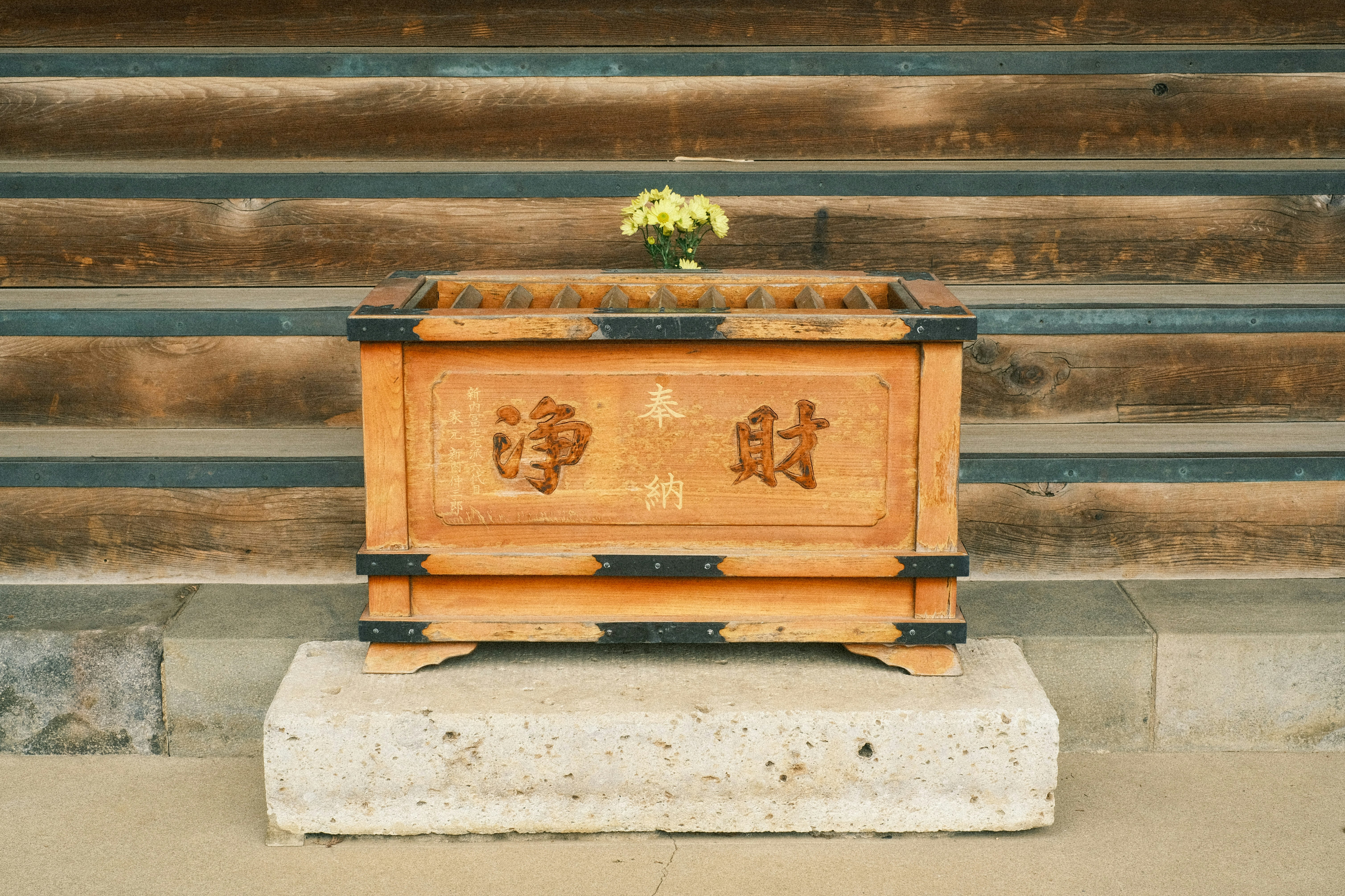 petite boîte de dons en bois sur un socle en pierre dans un cadre de temple