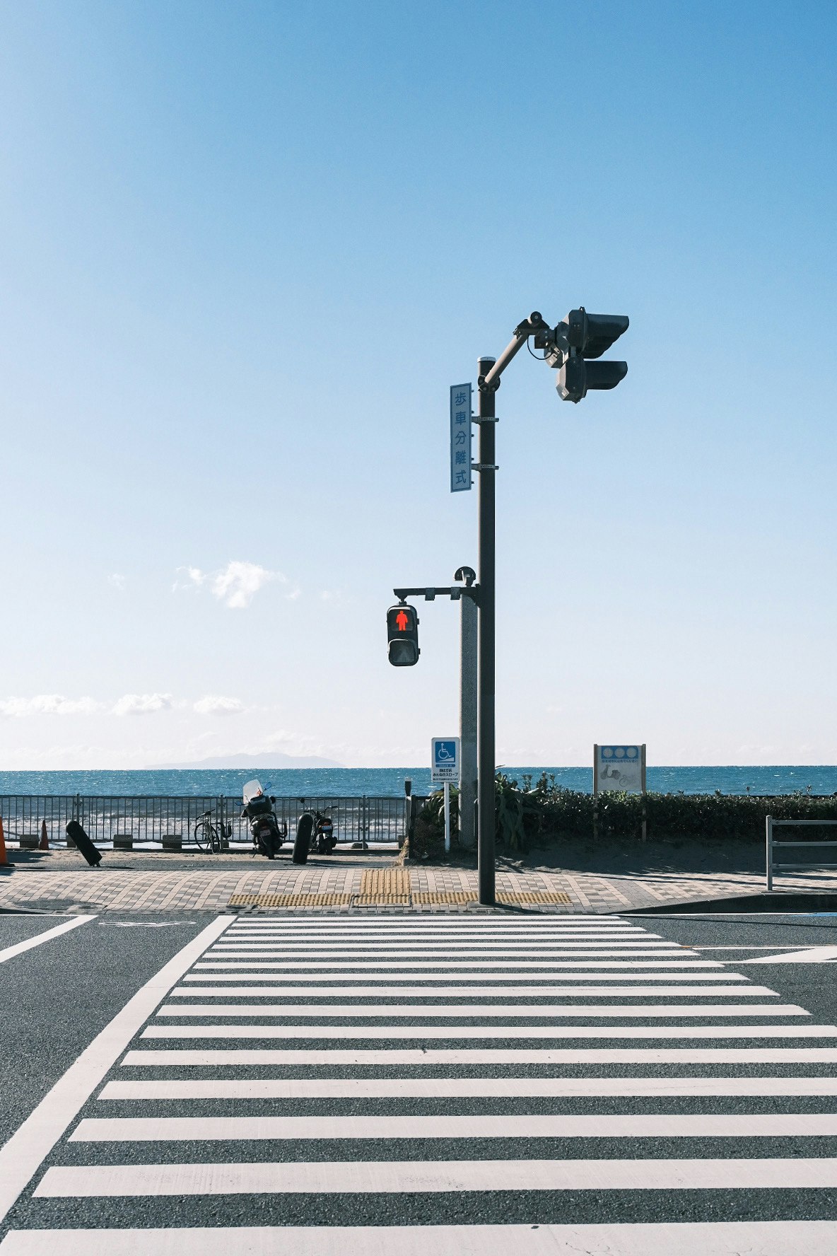 海辺の横断歩道と赤信号、青空の下の交差点