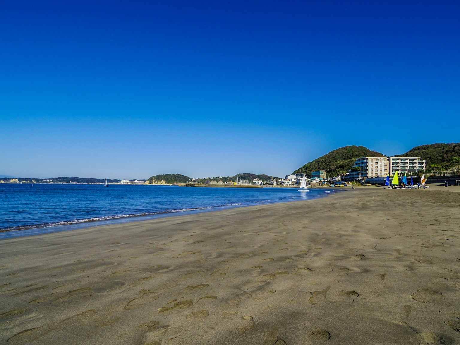 Strandszene mit klarem blauen Himmel und Ozean Sandstrand mit entfernten Gebäuden
