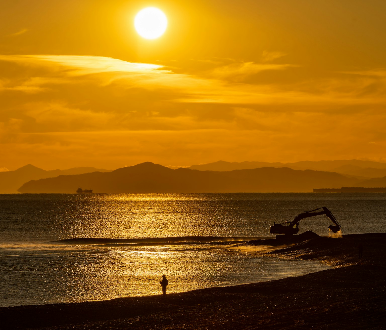 Silhouette di una persona sulla spiaggia con una macchina da costruzione al tramonto