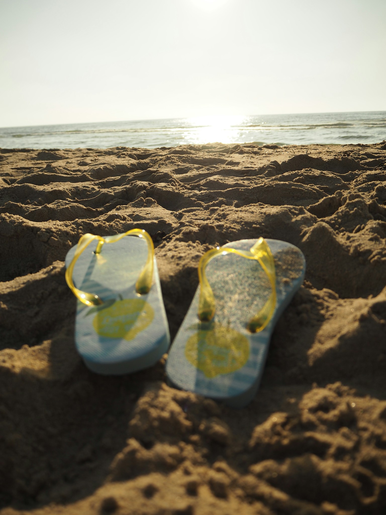 Yellow flip flops on sandy beach with ocean background
