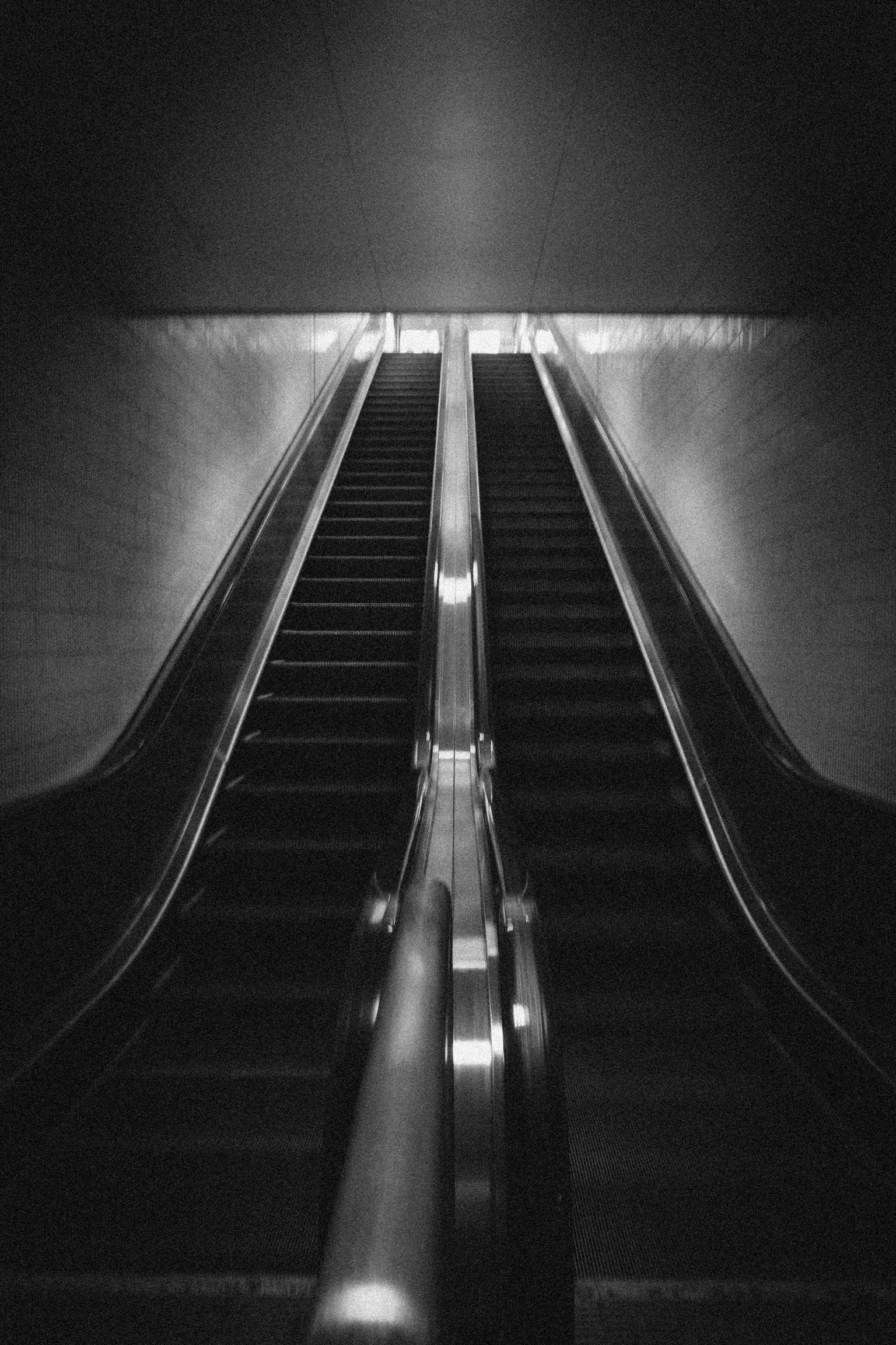 Schwarzweißbild einer Rolltreppe, die mit Metallhandläufen und hellem Licht nach oben führt