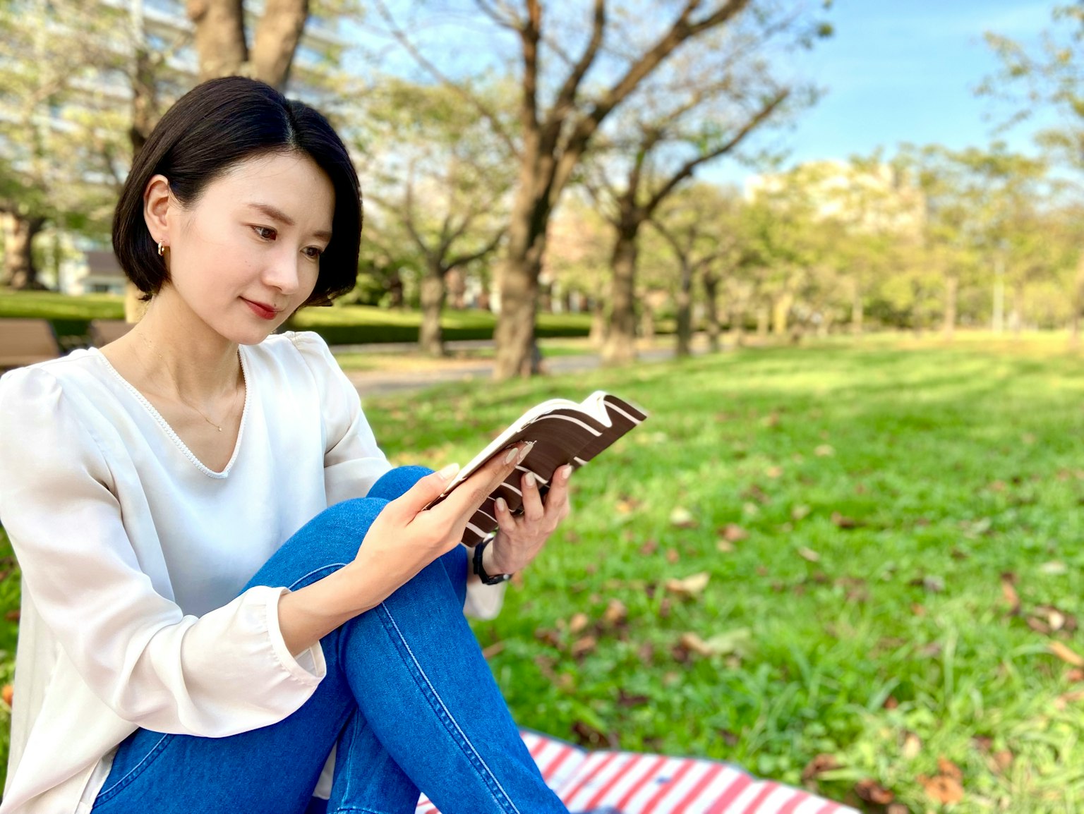 Wanita membaca buku di taman rumput hijau pohon musim gugur