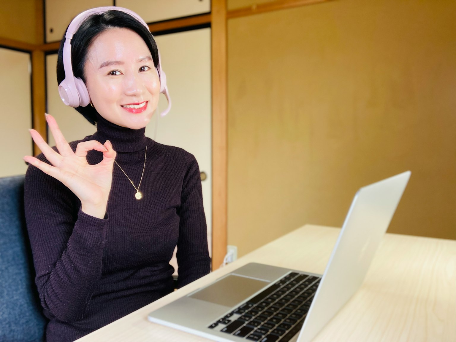 Una donna con un auricolare che sorride e fa un gesto di ok davanti a un laptop