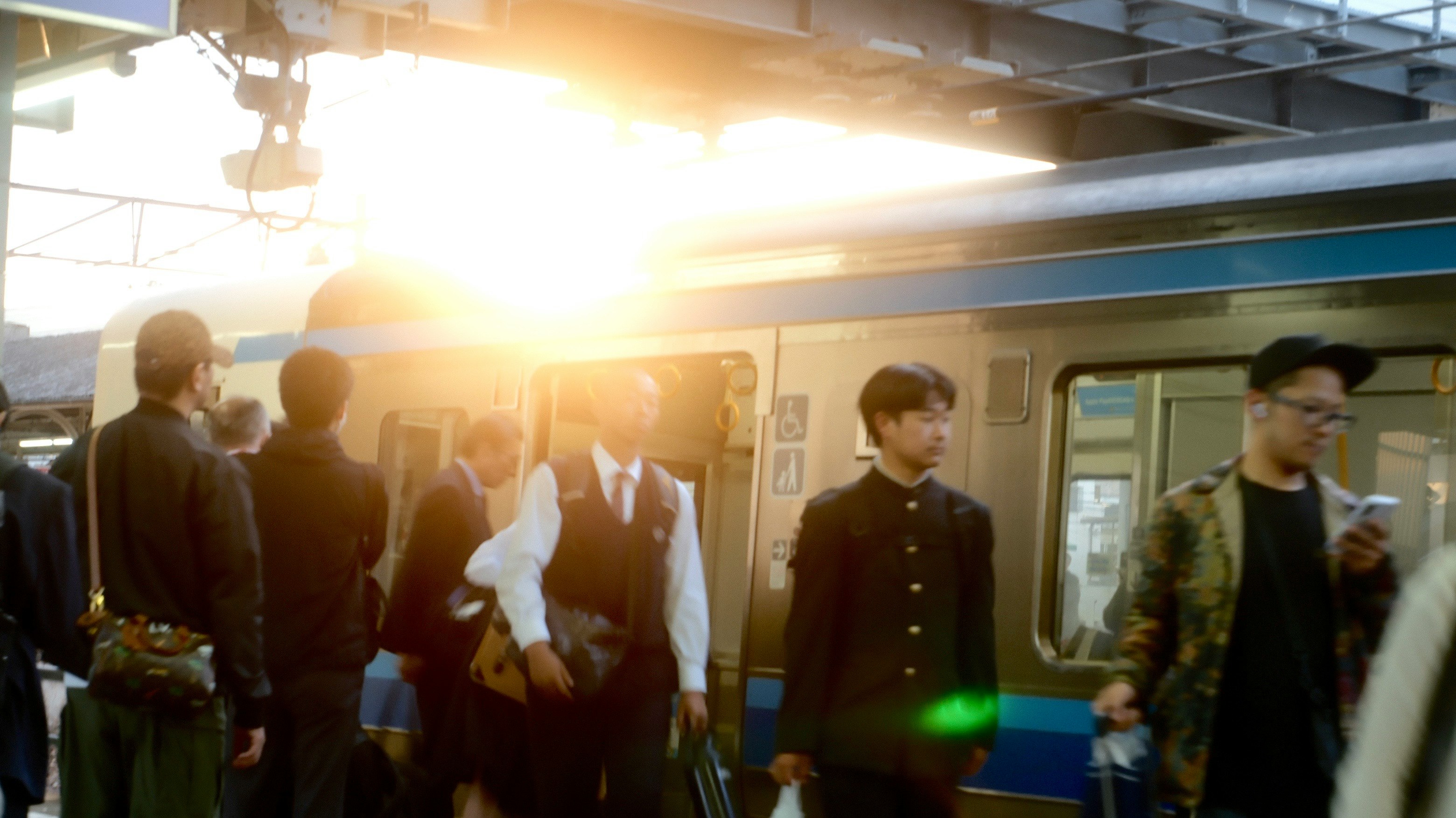 駅のホームでスーツ姿の人々と電車が並ぶ夕方の光