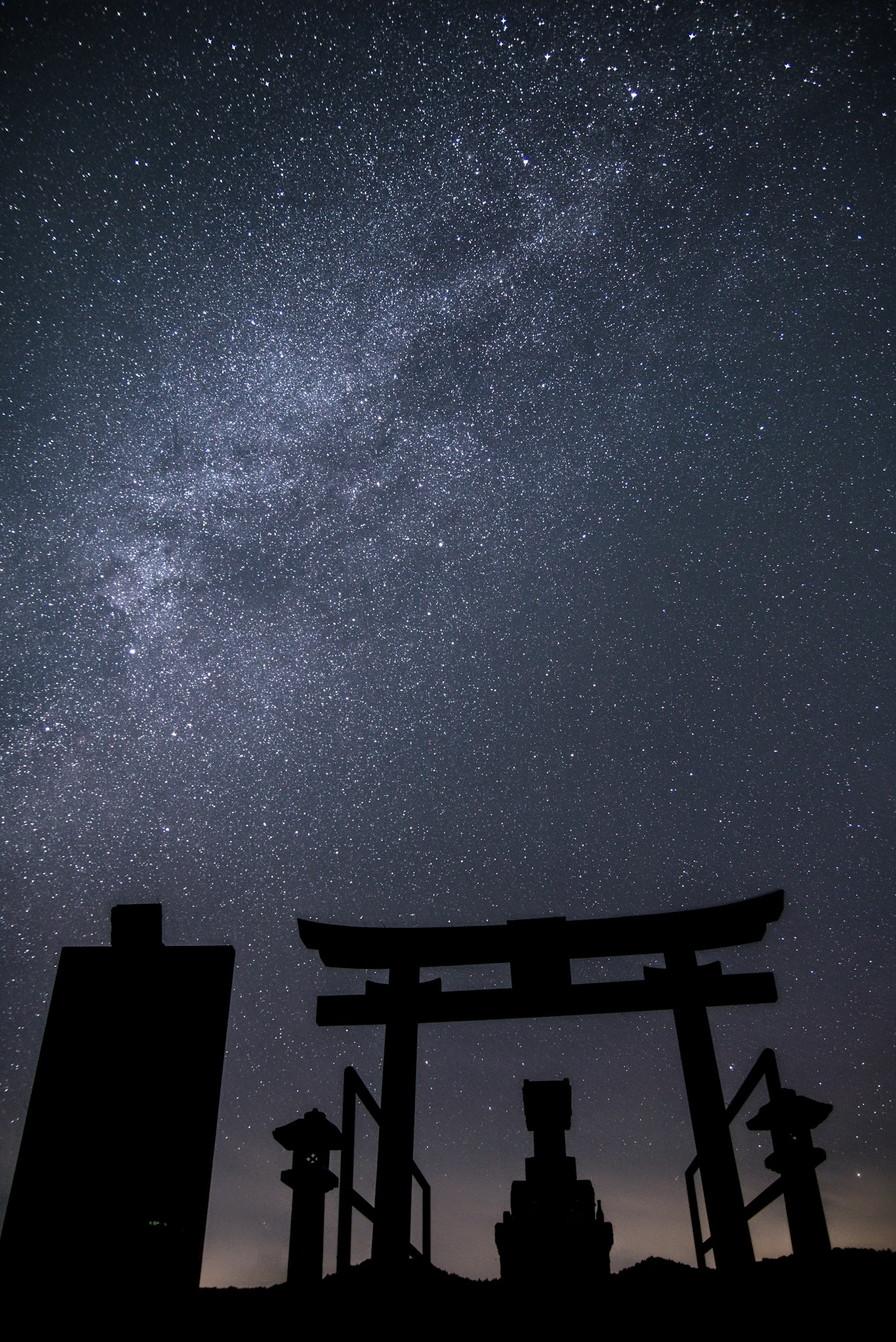 Silhouette of a torii gate under a starry sky with buildings