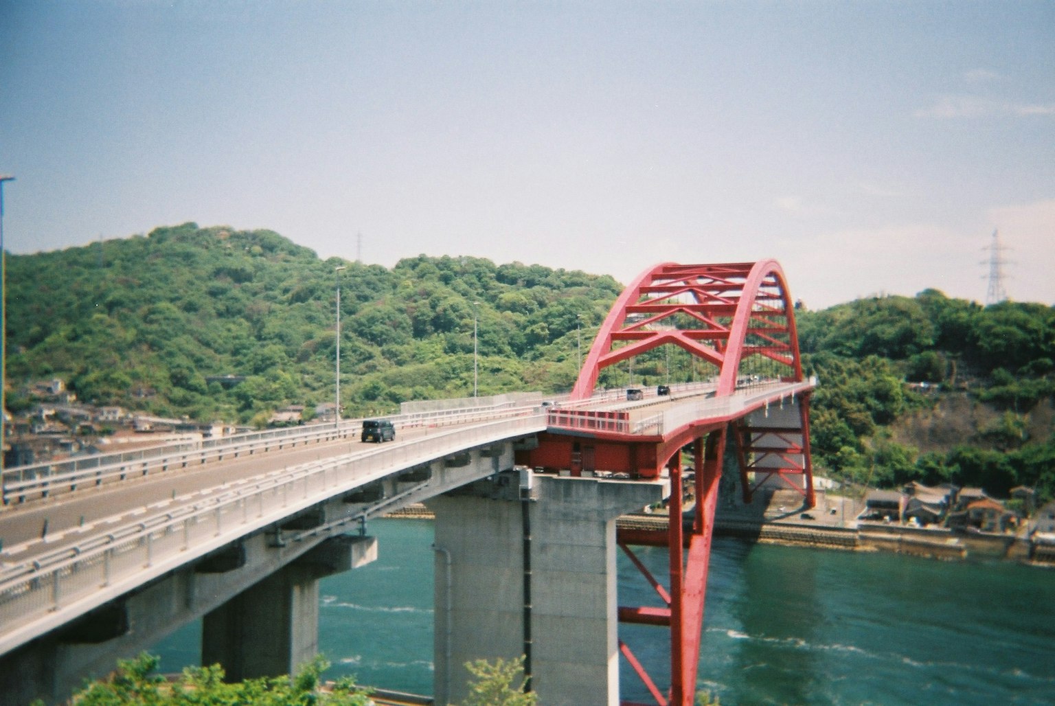 Red arch bridge spanning over a river with lush green hills in the background