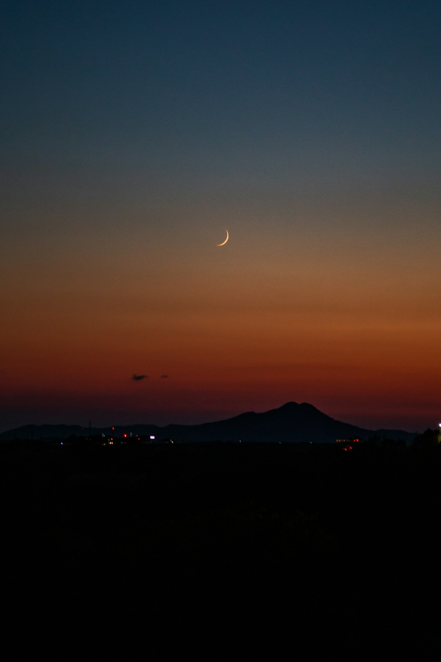 Una luna crescente nel cielo crepuscolare su un paesaggio montano