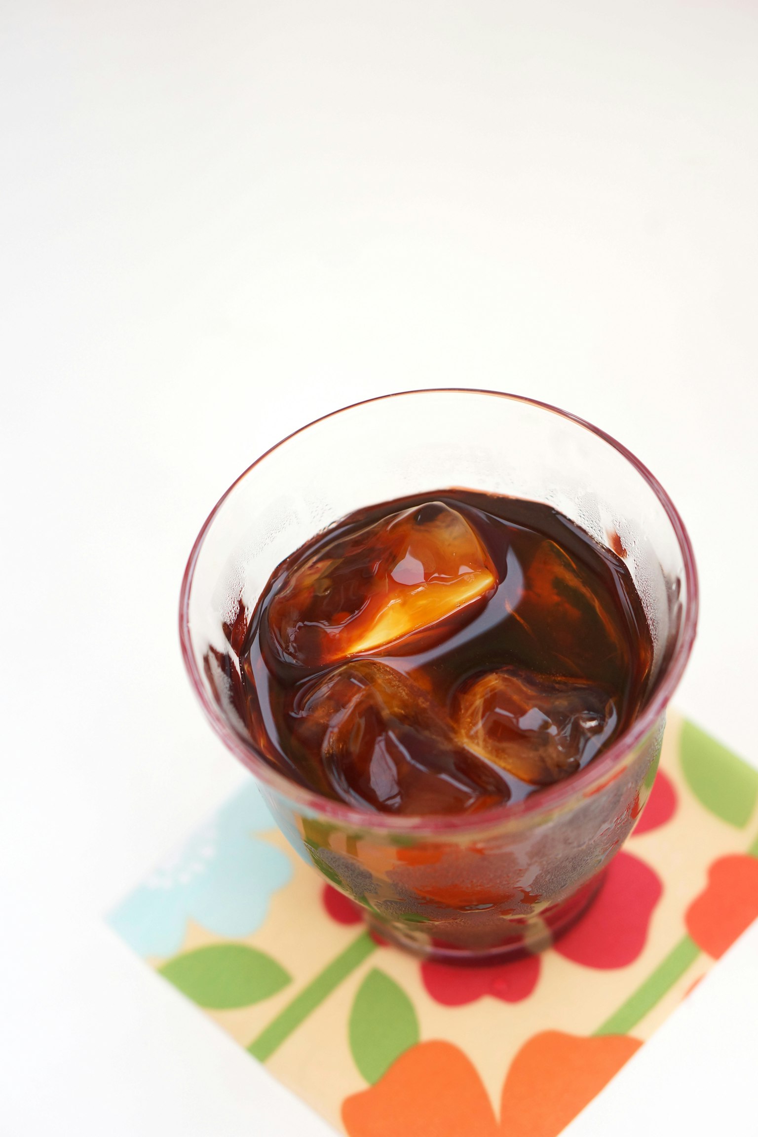 Un bicchiere di tè freddo con cubetti di ghiaccio e una fetta d'arancia sopra posato su un sottobicchiere colorato