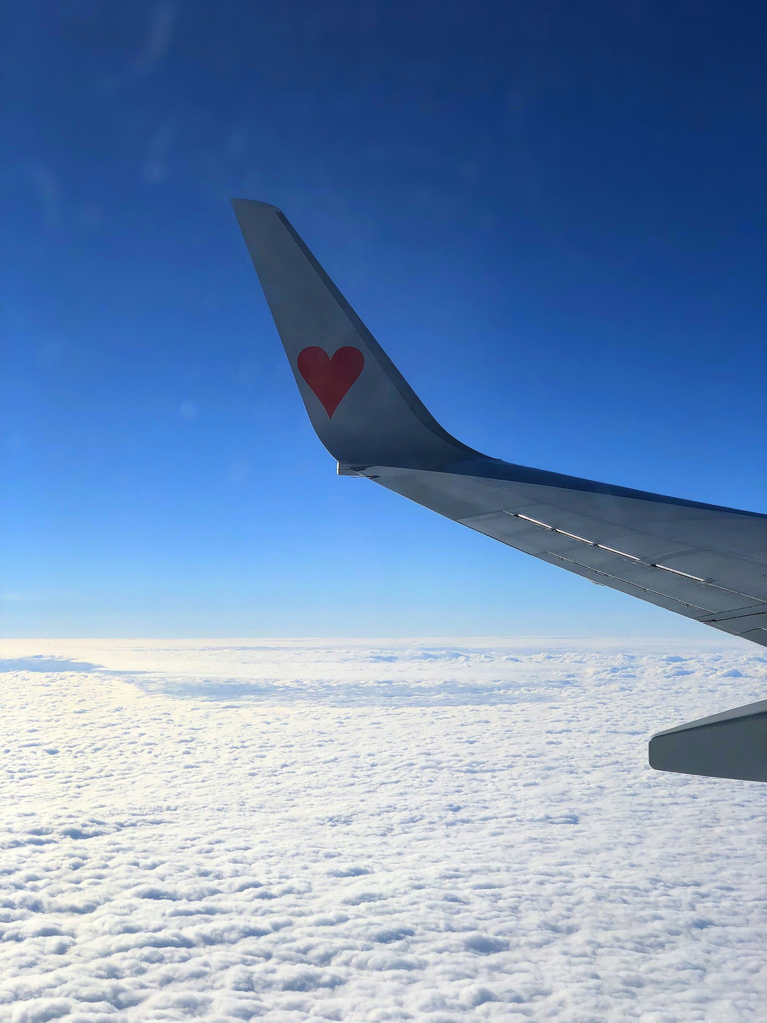Aile d'avion avec un logo de cœur rouge sur fond de ciel bleu et de nuages