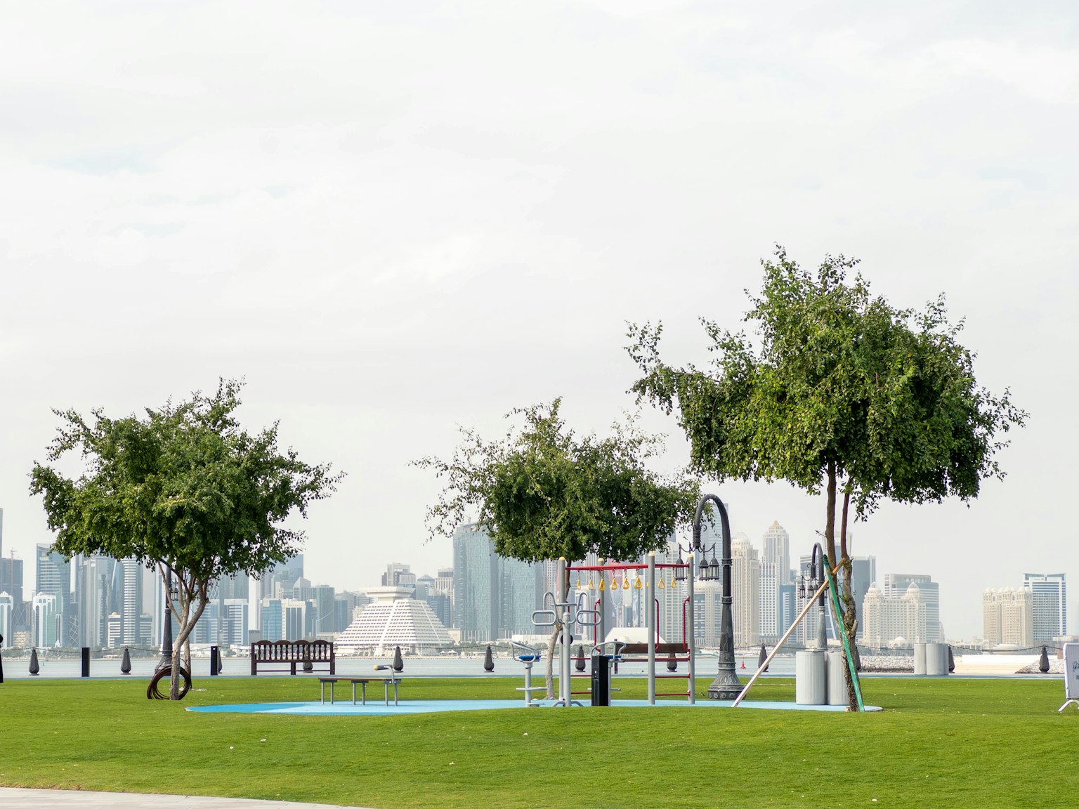 Parkszene mit grünen Bäumen und Spielgeräten mit einer Stadtsilhouette im Hintergrund