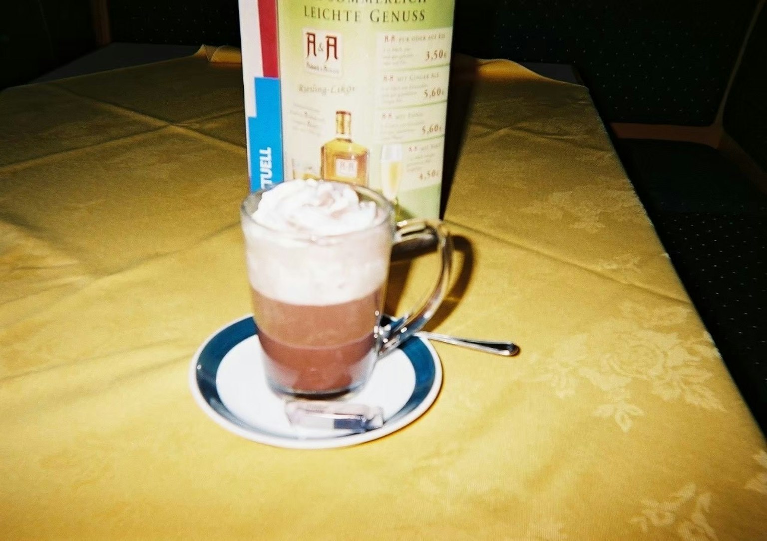 A glass of hot chocolate topped with whipped cream on a yellow tablecloth