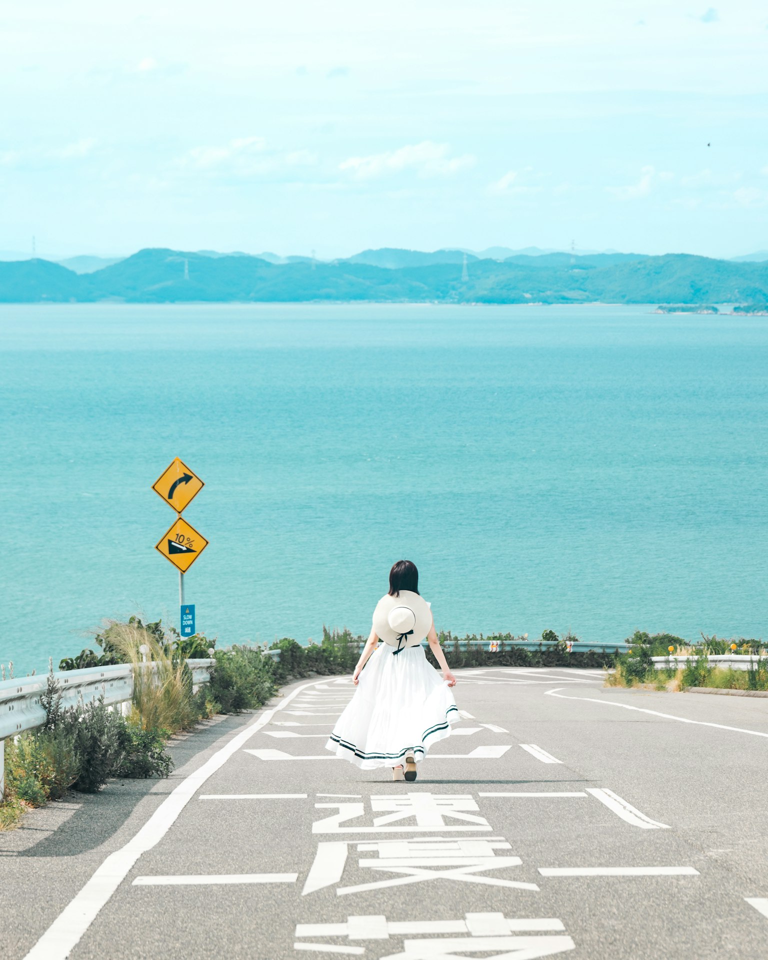 一位穿著白色長裙的女性在道路上走向大海