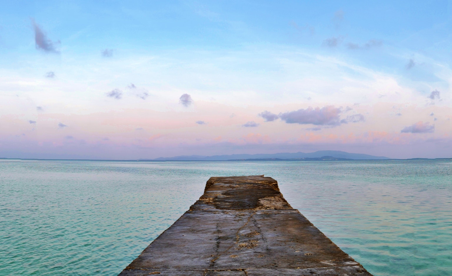 Vista escénica de un muelle que se extiende en aguas turquesas tranquilas bajo un cielo pastel