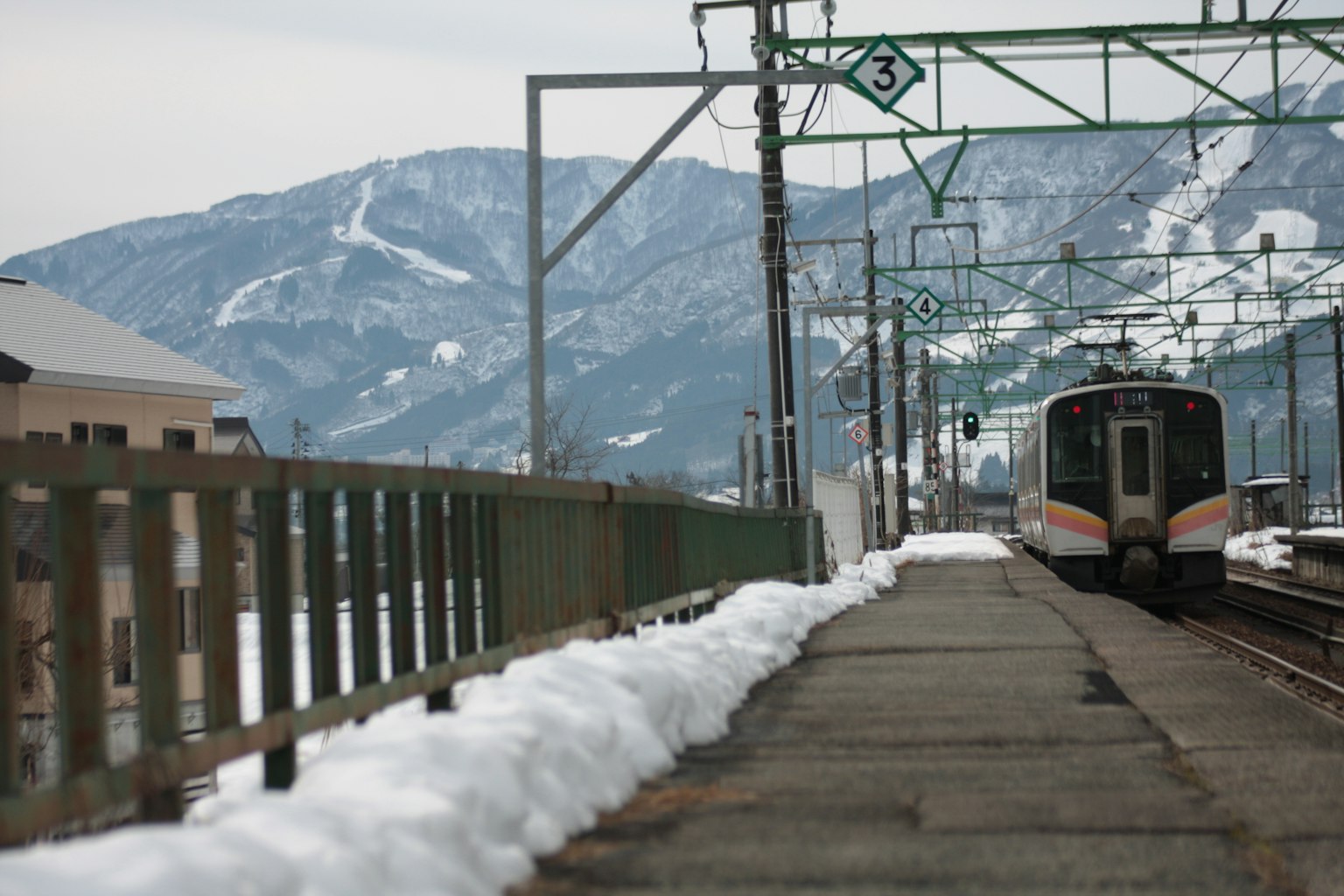 Treno in arrivo in una stazione innevata con montagne sullo sfondo