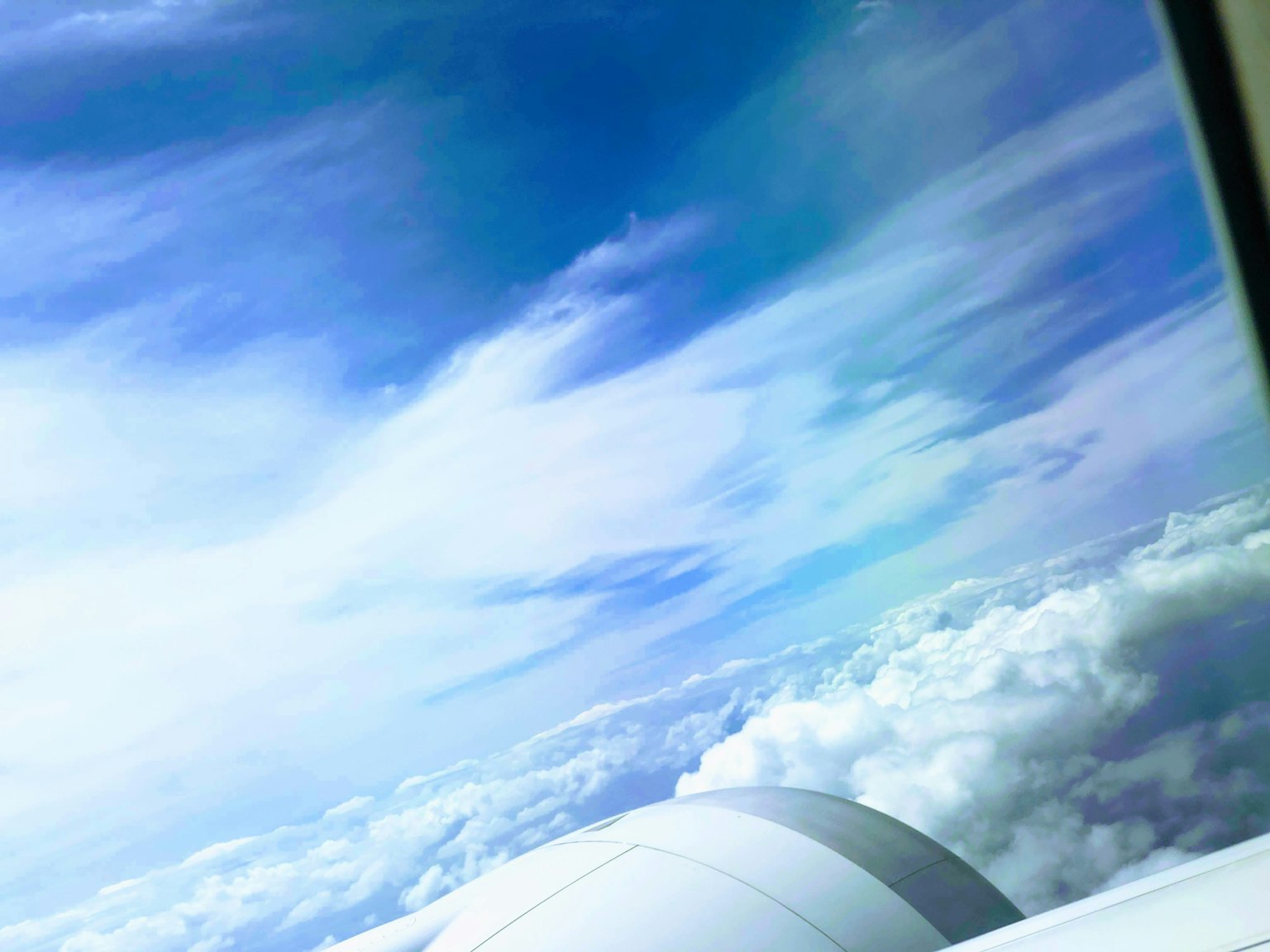 Blue sky above the clouds with a glimpse of an airplane wing