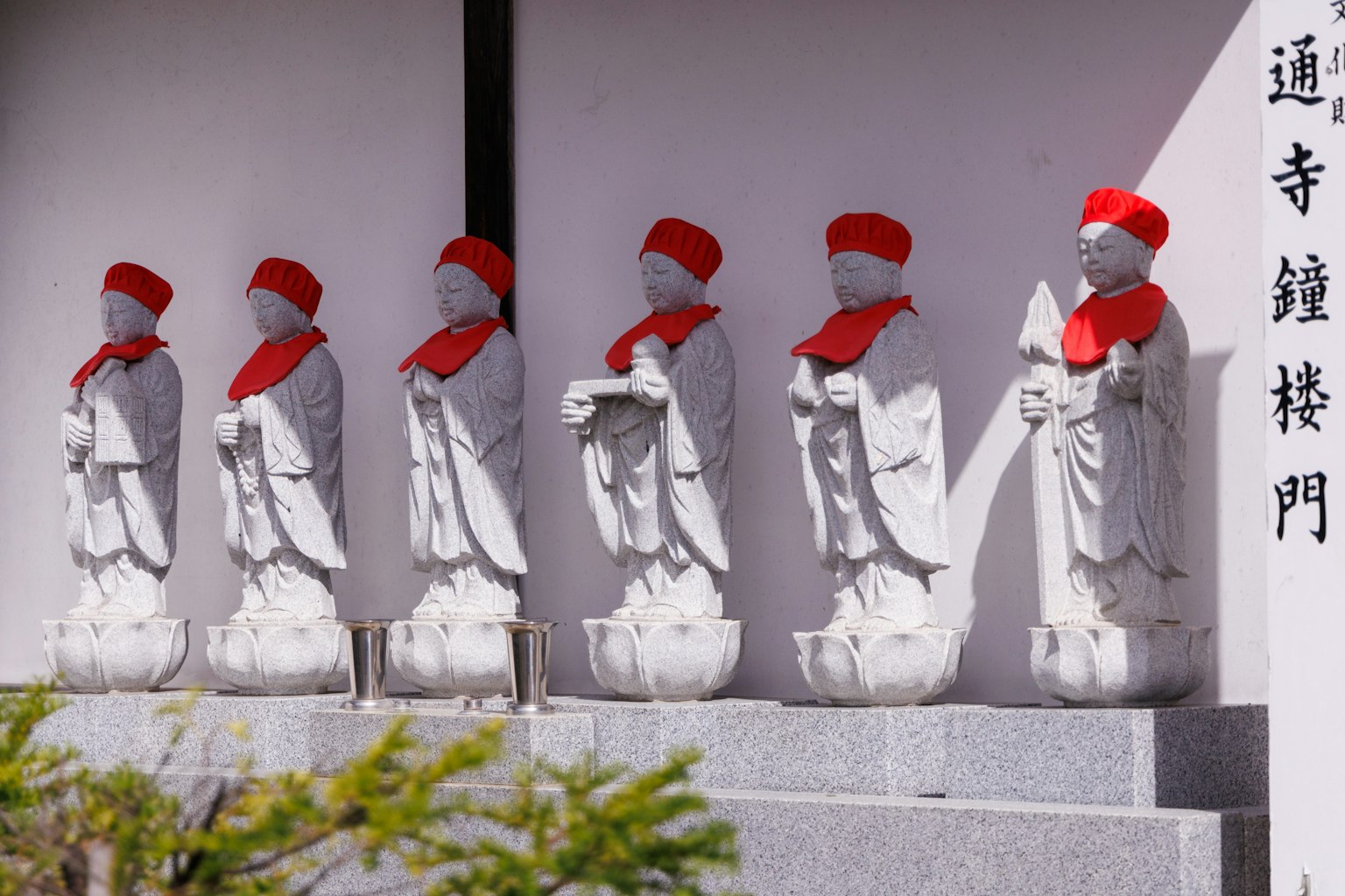 六个戴着红帽子的白色雕像排成一列在日本寺庙