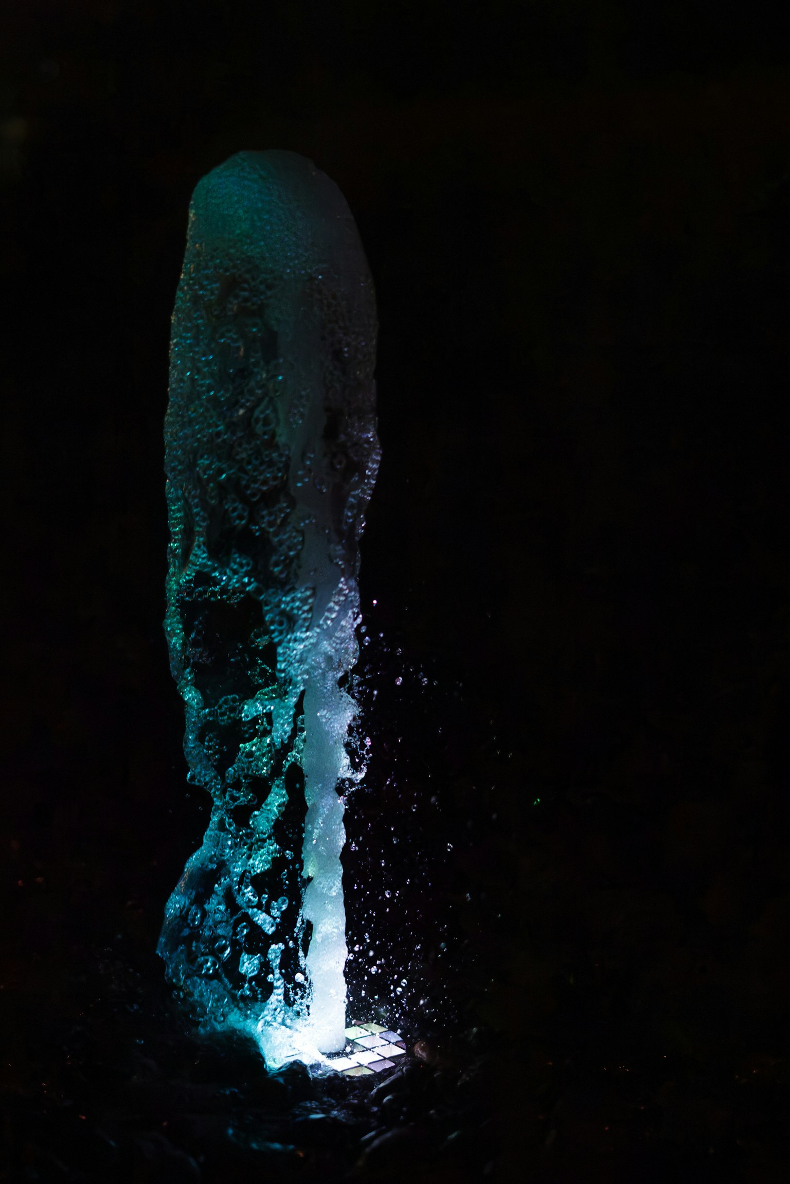 Water fountain illuminated by blue light against a dark background