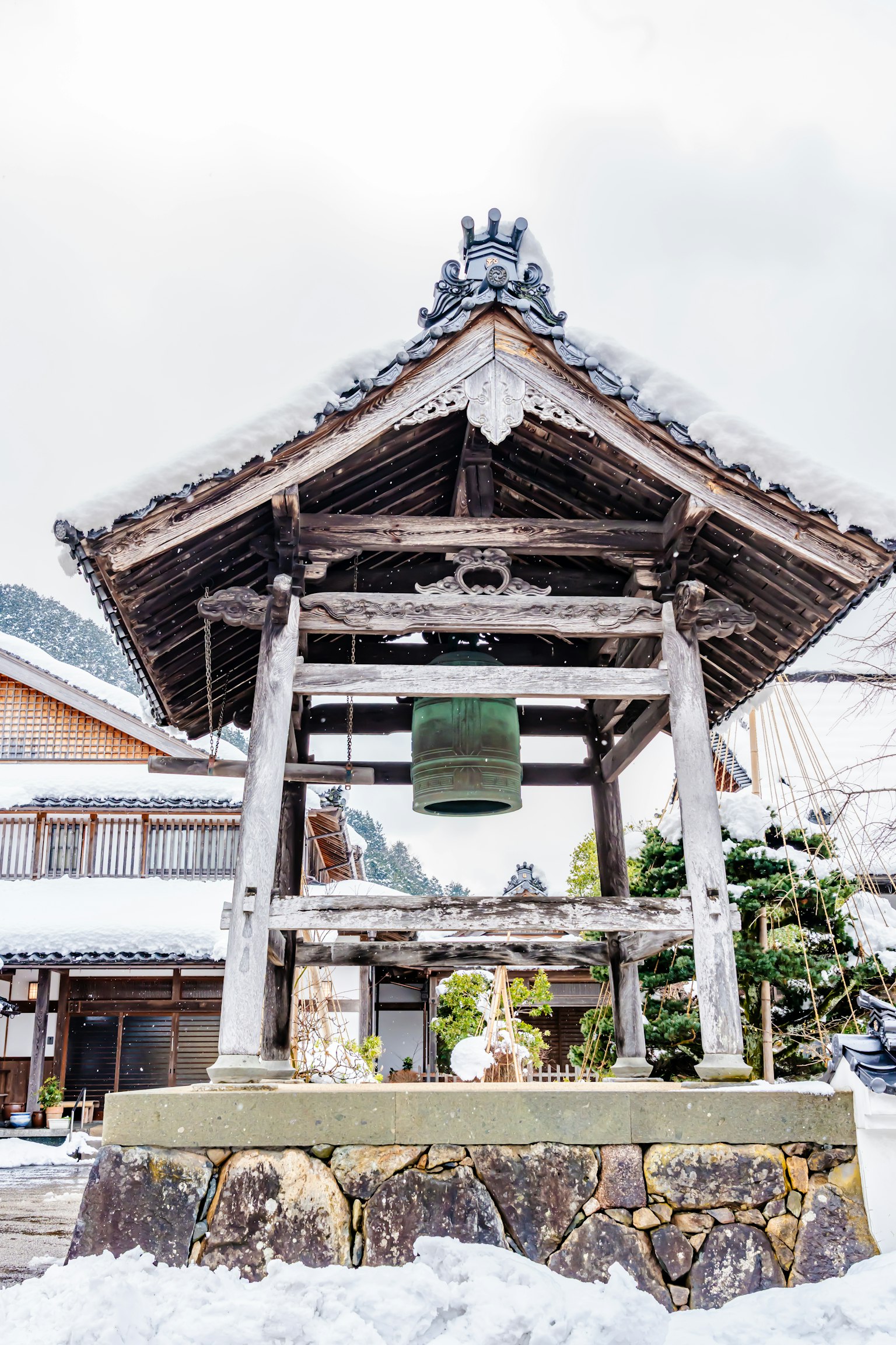 Traditioneller japanischer Glockenturm im Schnee mit Holzkonstruktion und grüner Glocke