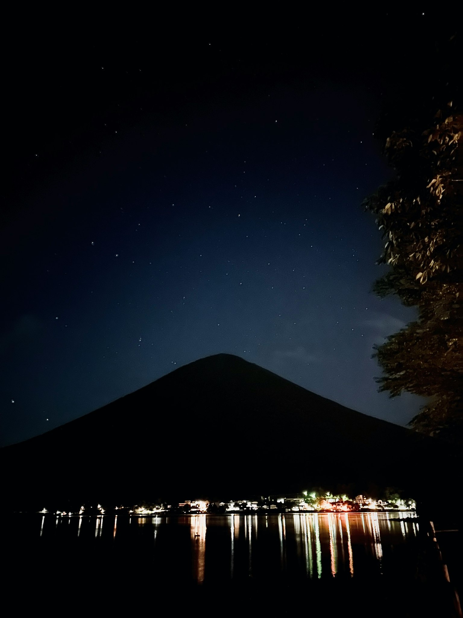 Silhouette di una montagna che si riflette su un lago calmo sotto un cielo stellato