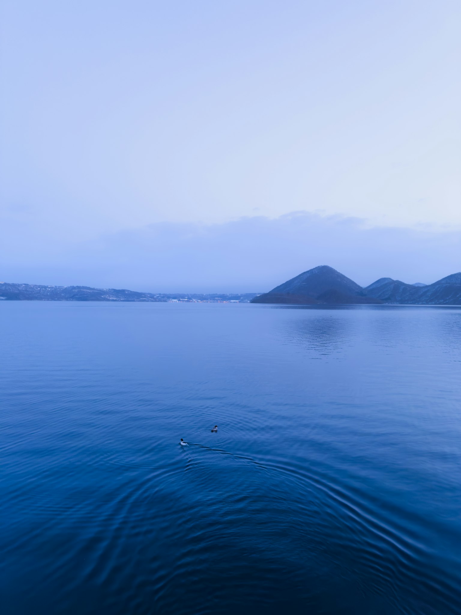Paysage de lac bleu calme avec des silhouettes de montagnes au loin