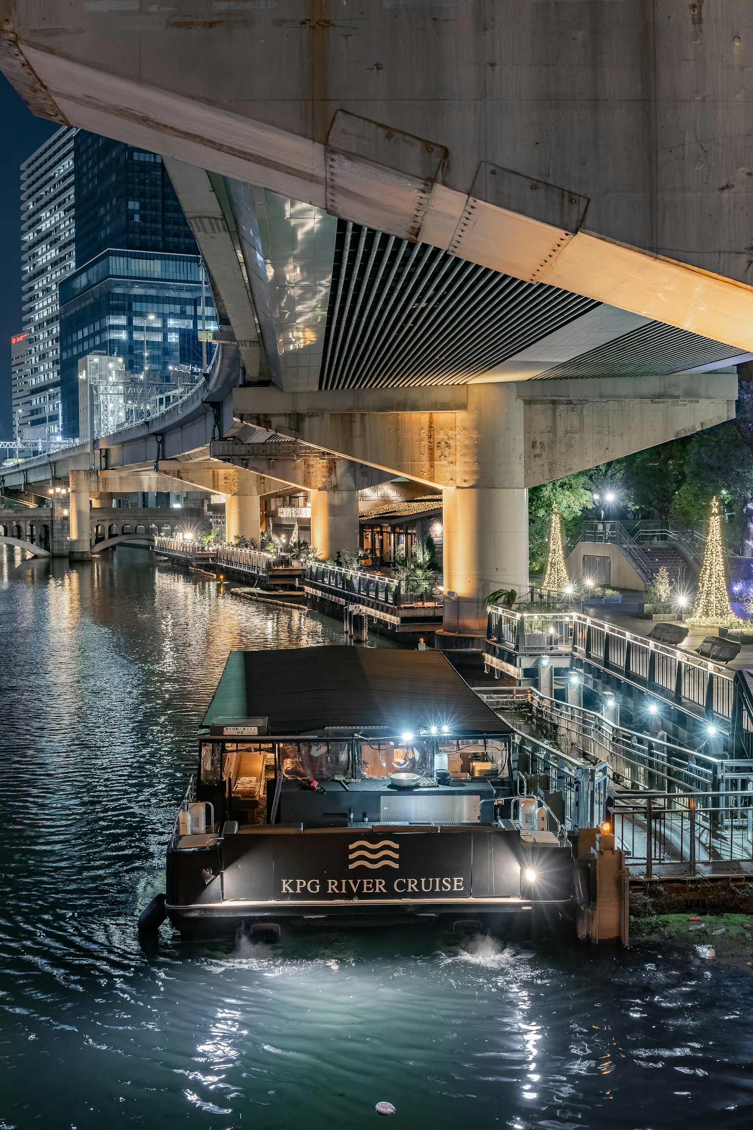 เรือที่จอดอยู่ริมแม่น้ำในเวลากลางคืนพร้อมตึกระฟ้าในพื้นหลัง