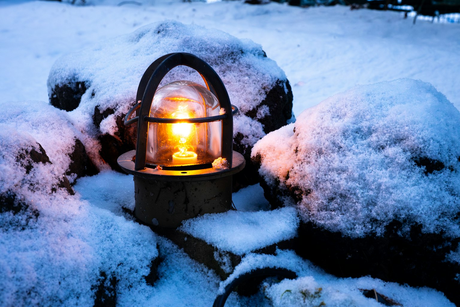 A lantern emitting warm light sitting on snow-covered rocks