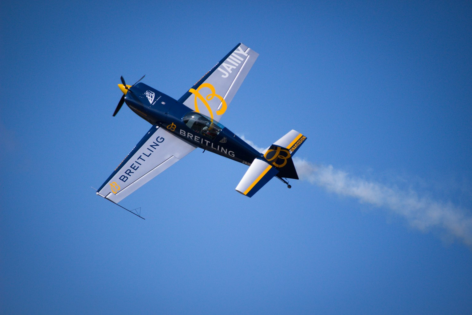 A blue aircraft flying upside down against a clear blue sky