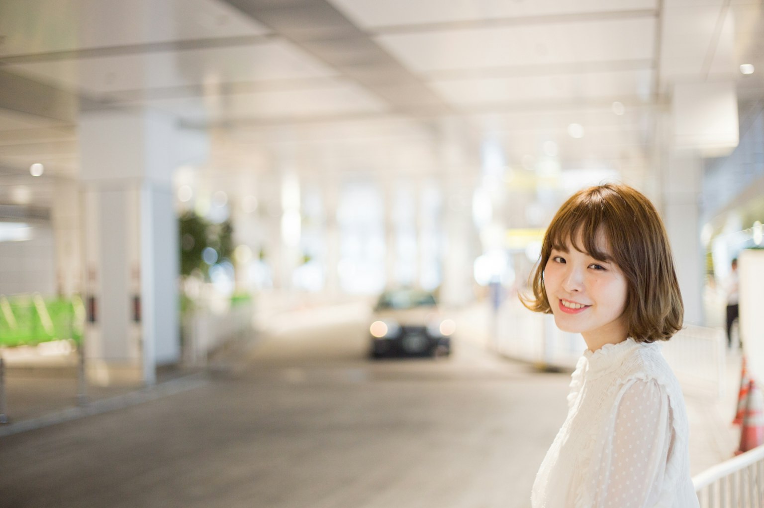 明るい場所で微笑む女性のポートレート 背景にはぼやけた車と緑の椅子