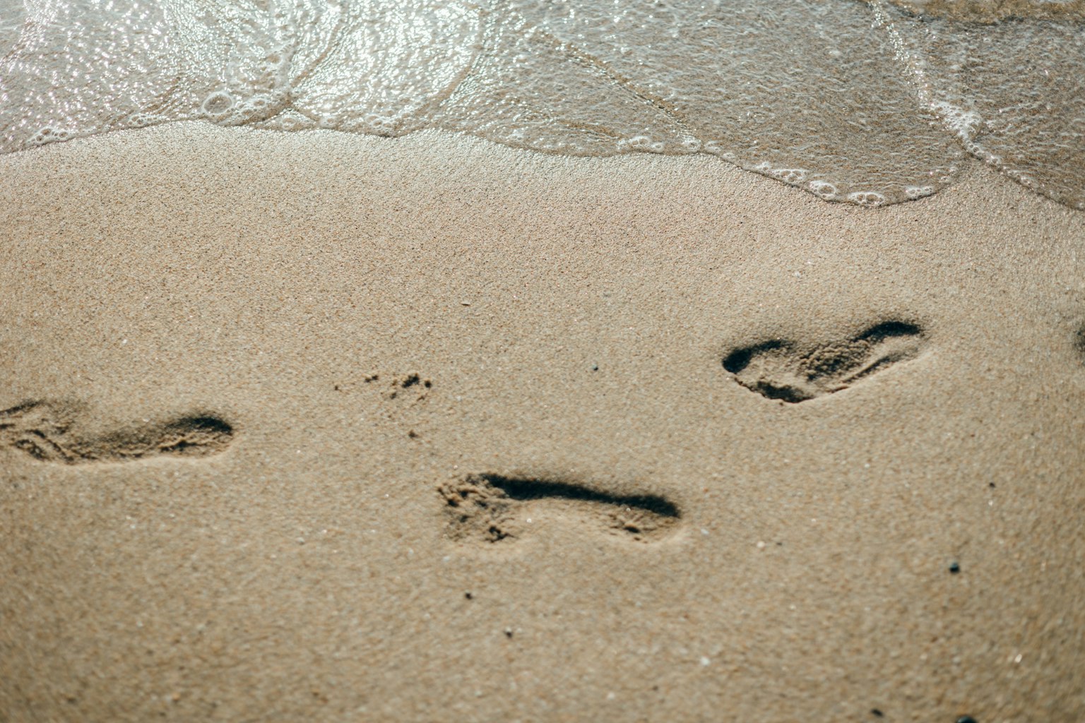 Jejak kaki di pantai berpasir dengan ombak lembut