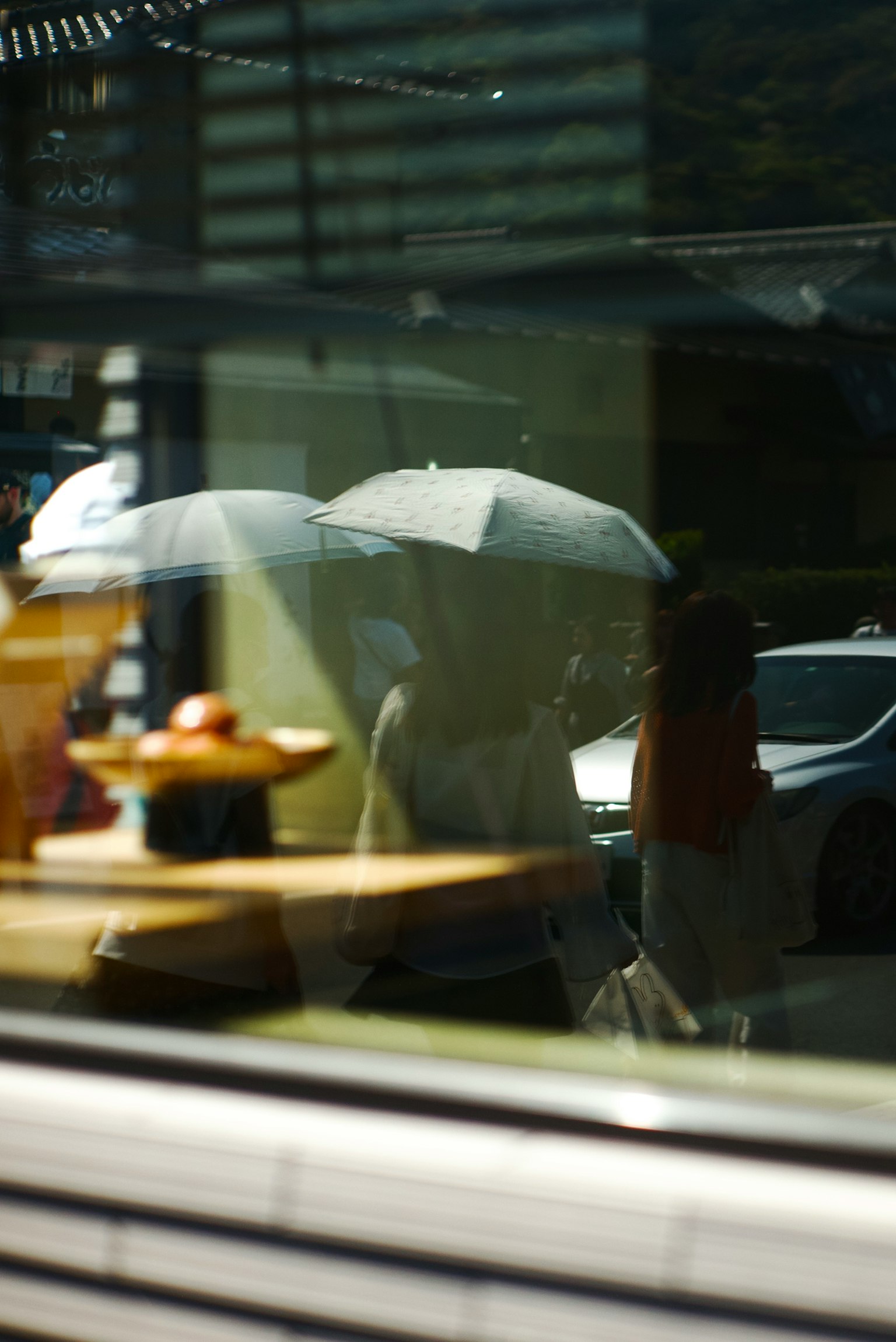 Reflection in a window showing people with umbrellas and desserts on a table