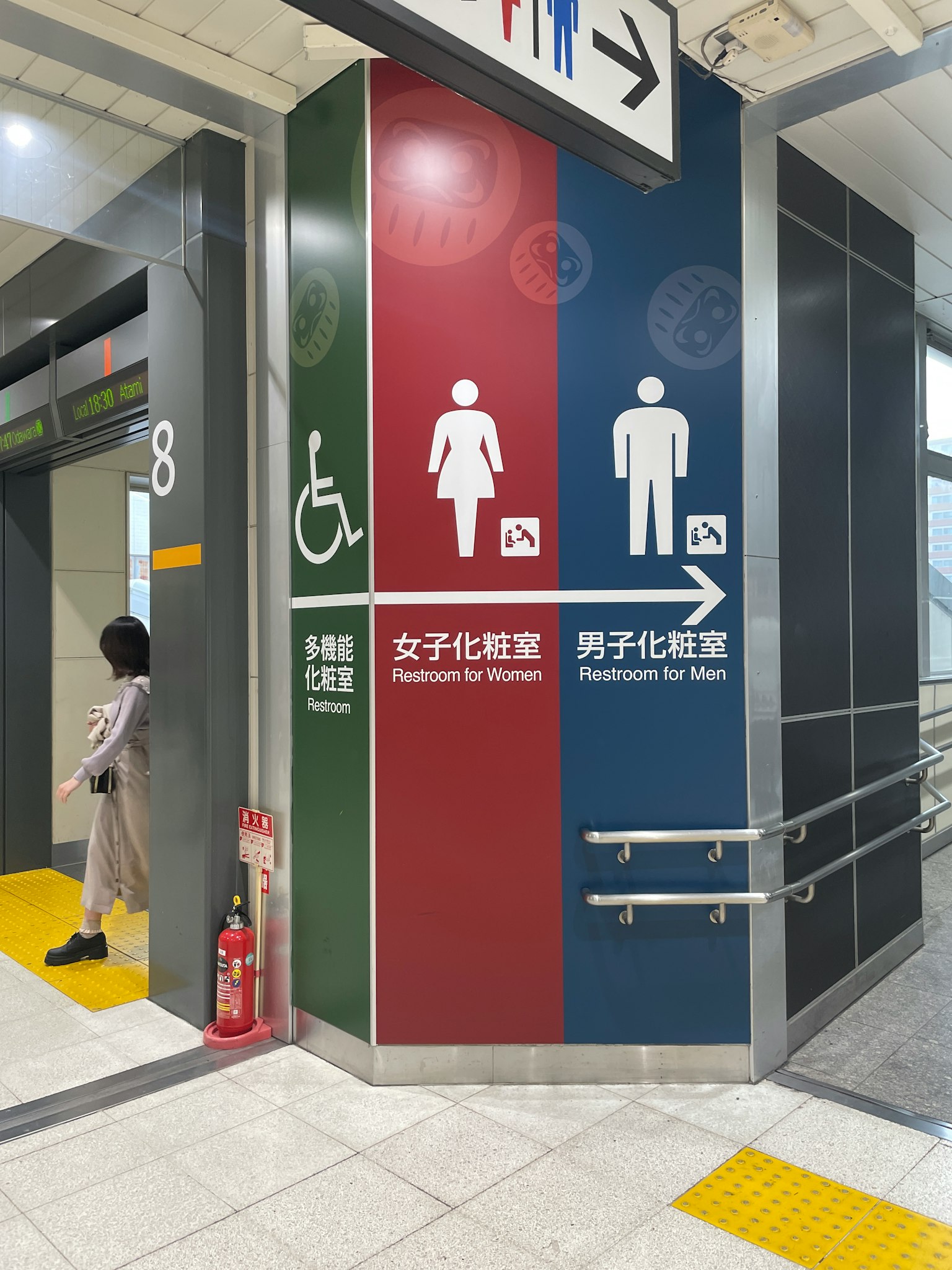 一位女性站在牆上的洗手間標誌旁邊