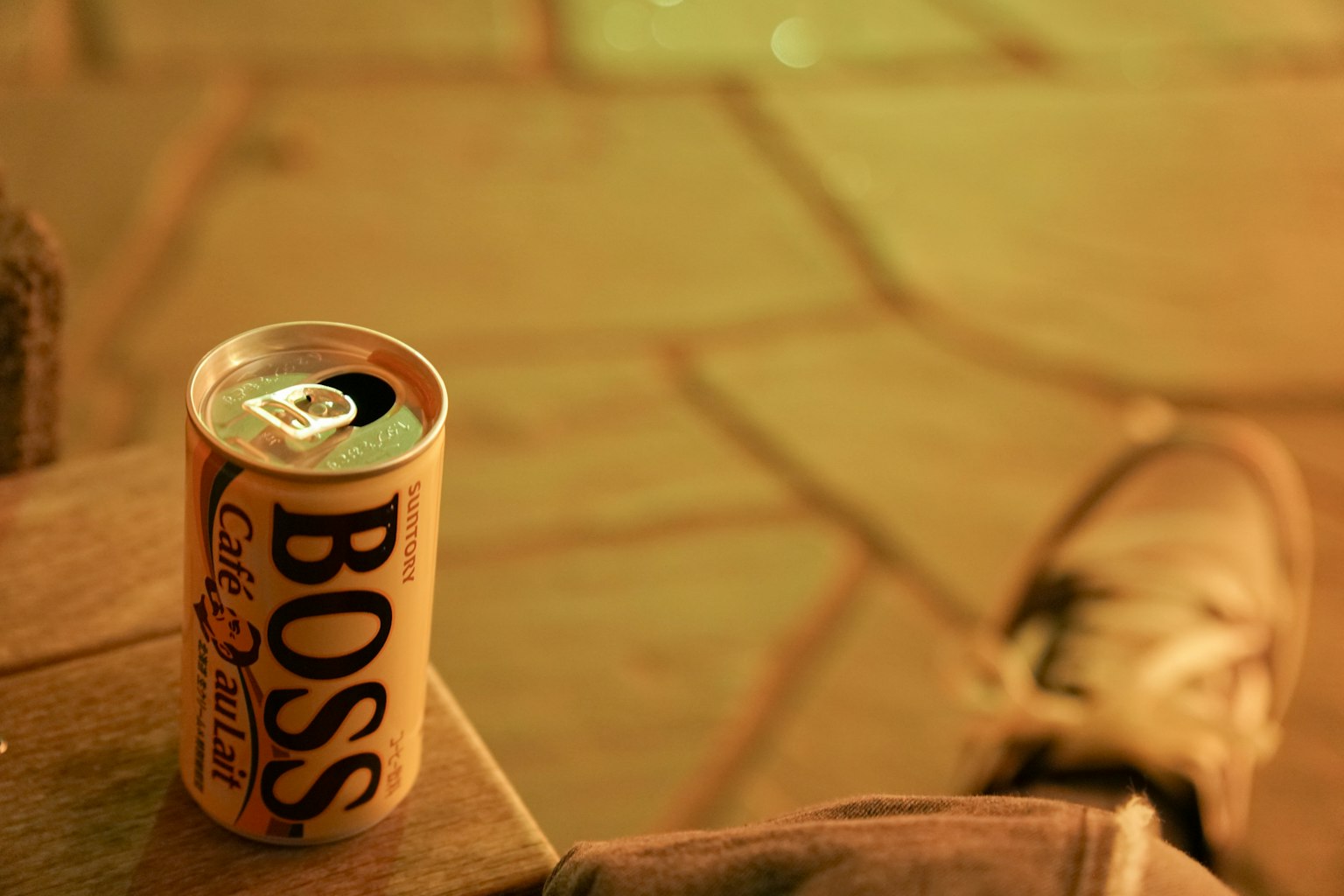 Una lata de café Boss colocada sobre una superficie con un tono naranja cálido junto a una zapatilla