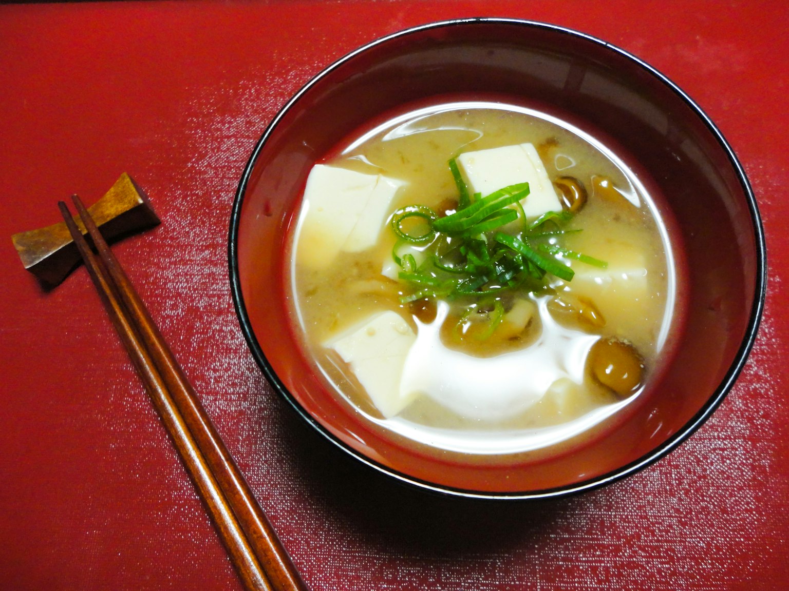 Bát súp miso với đậu phụ và hành lá trên nền đỏ