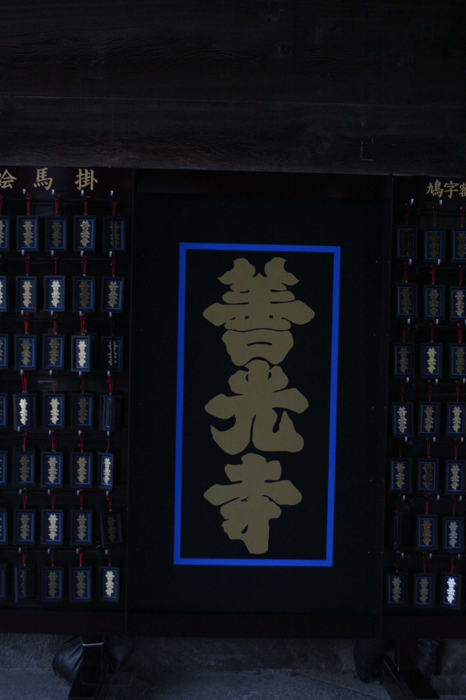 A sign with golden characters on a black background surrounded by neatly arranged small bottles