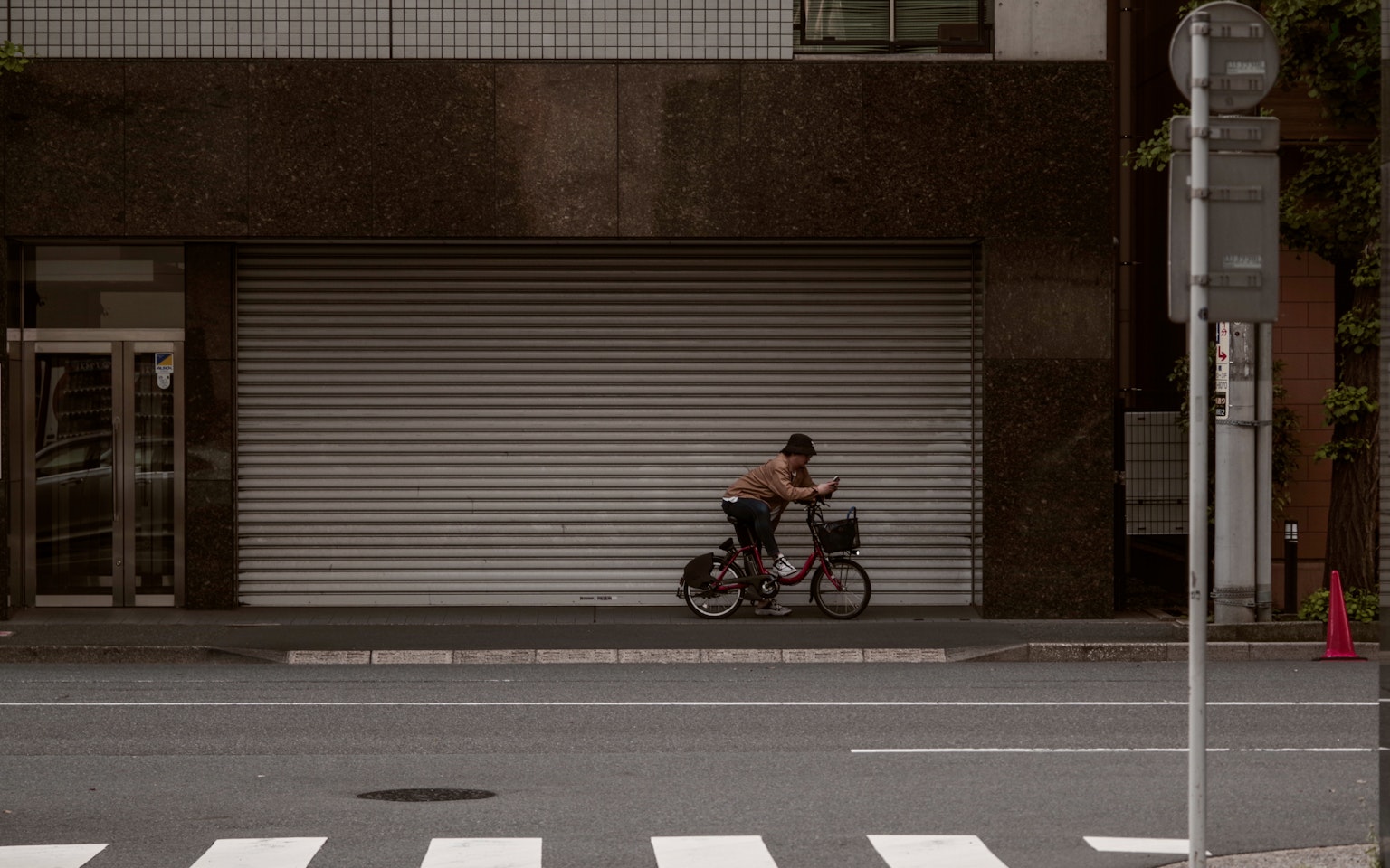 A person riding a bicycle in front of a closed storefront with a rolling shutter