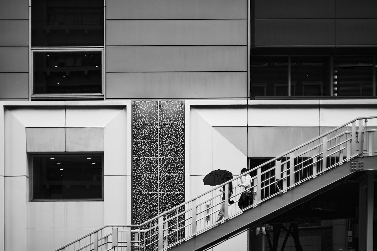 Coppia che sale una scala con un ombrello davanti a un edificio moderno in bianco e nero