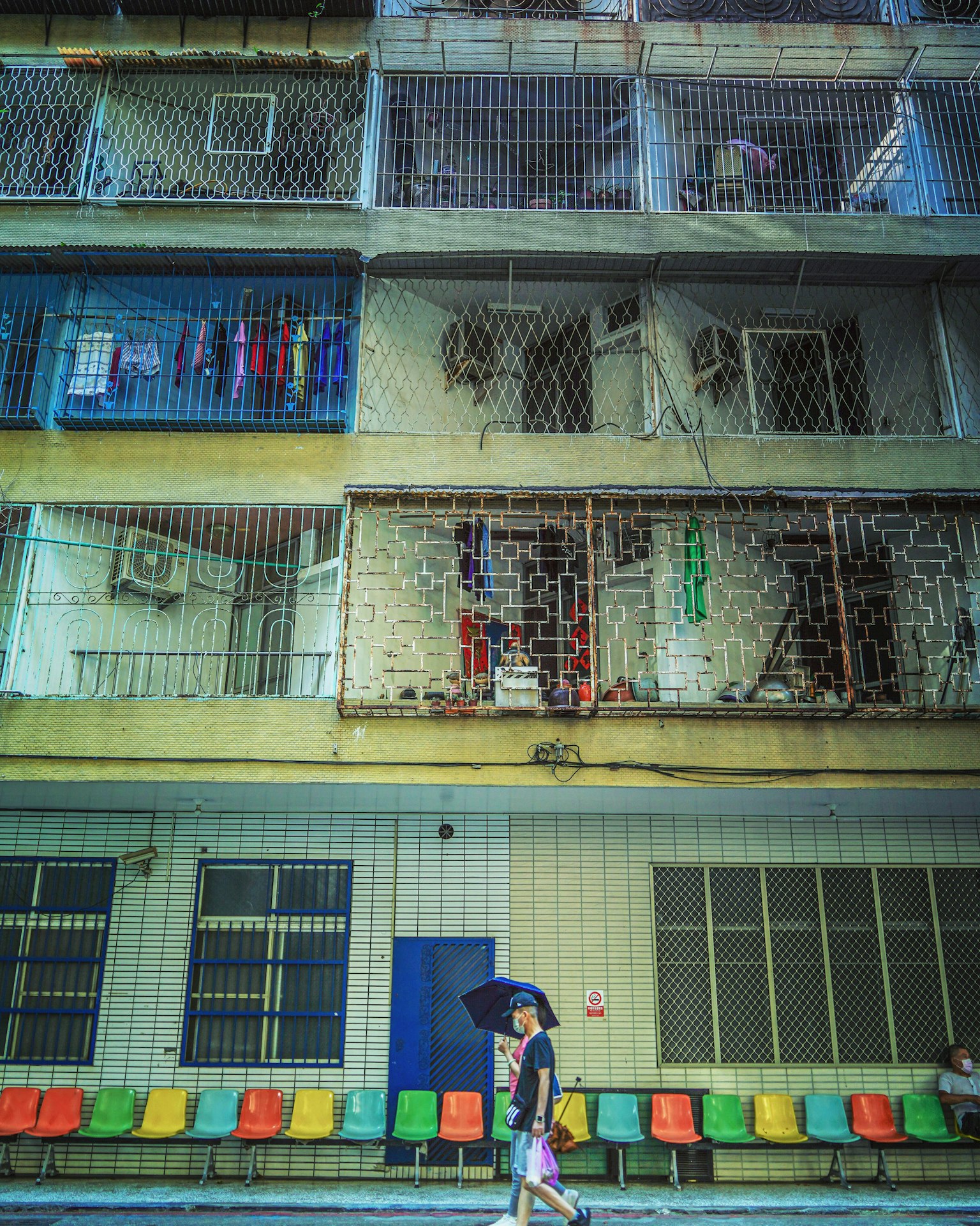 Une femme marchant devant un immeuble d'appartements avec des balcons bleus et des chaises colorées