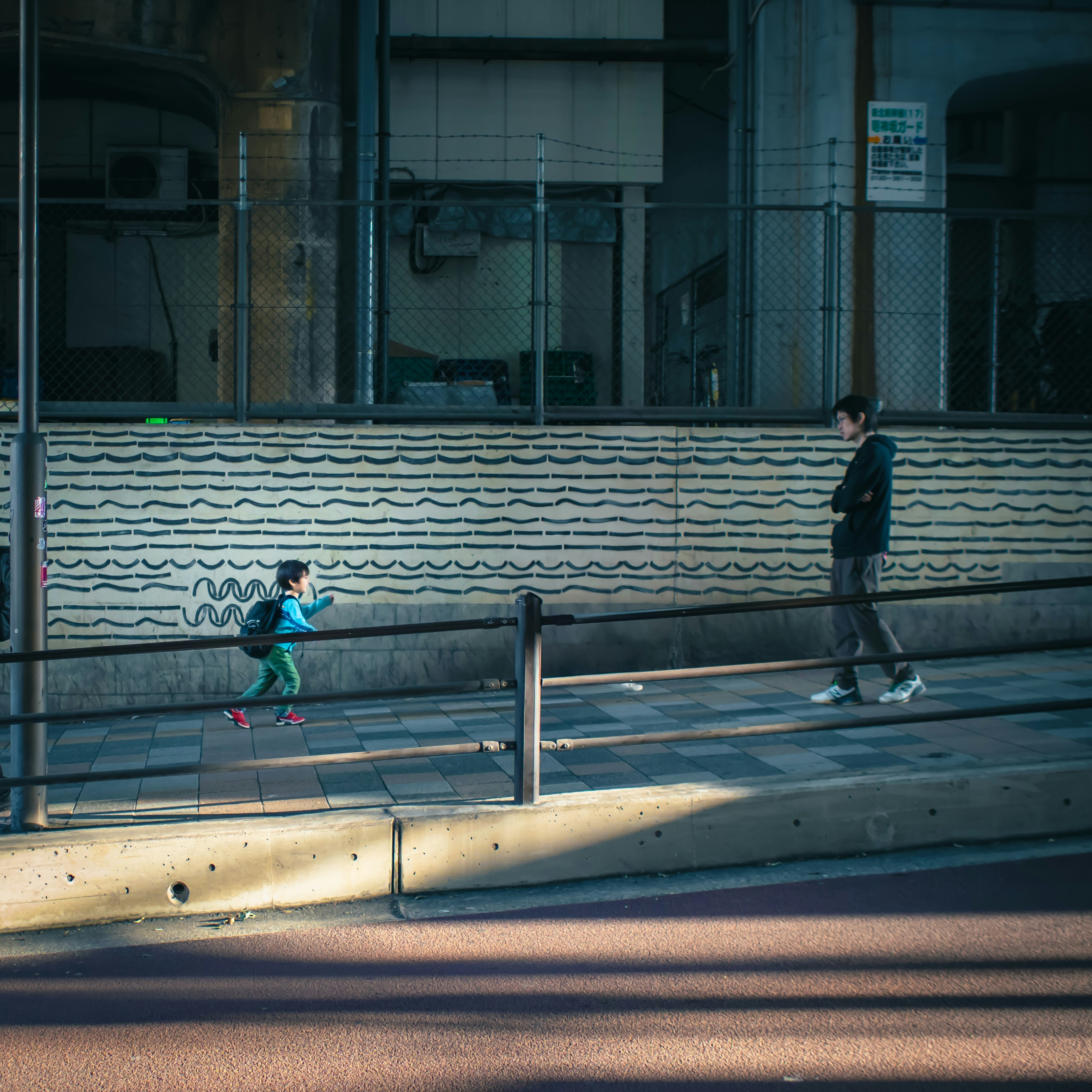 street corner under an elevated rail with a child running and an adult watching