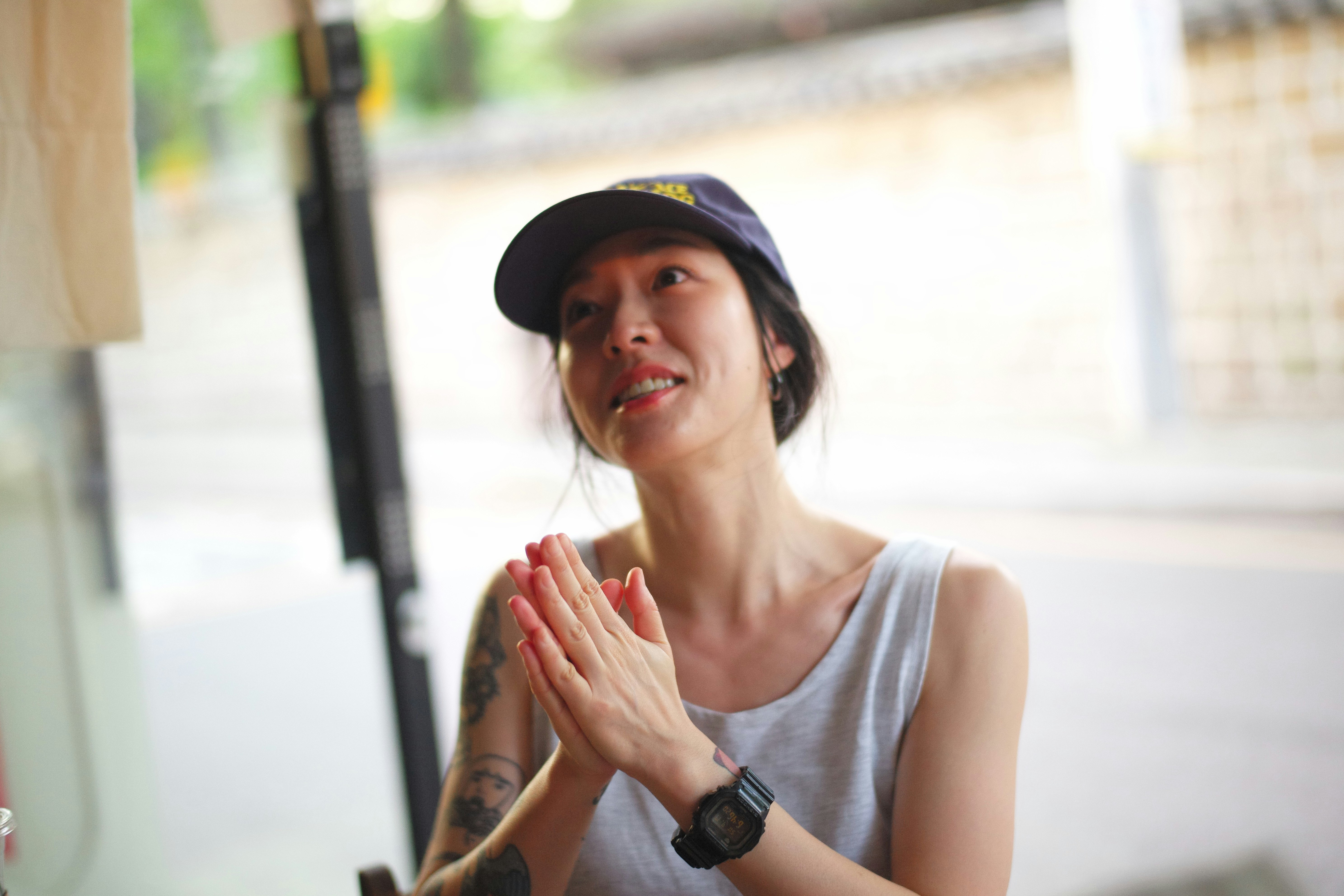 帽子をかぶった女性が手を合わせて微笑む屋外のスナップ