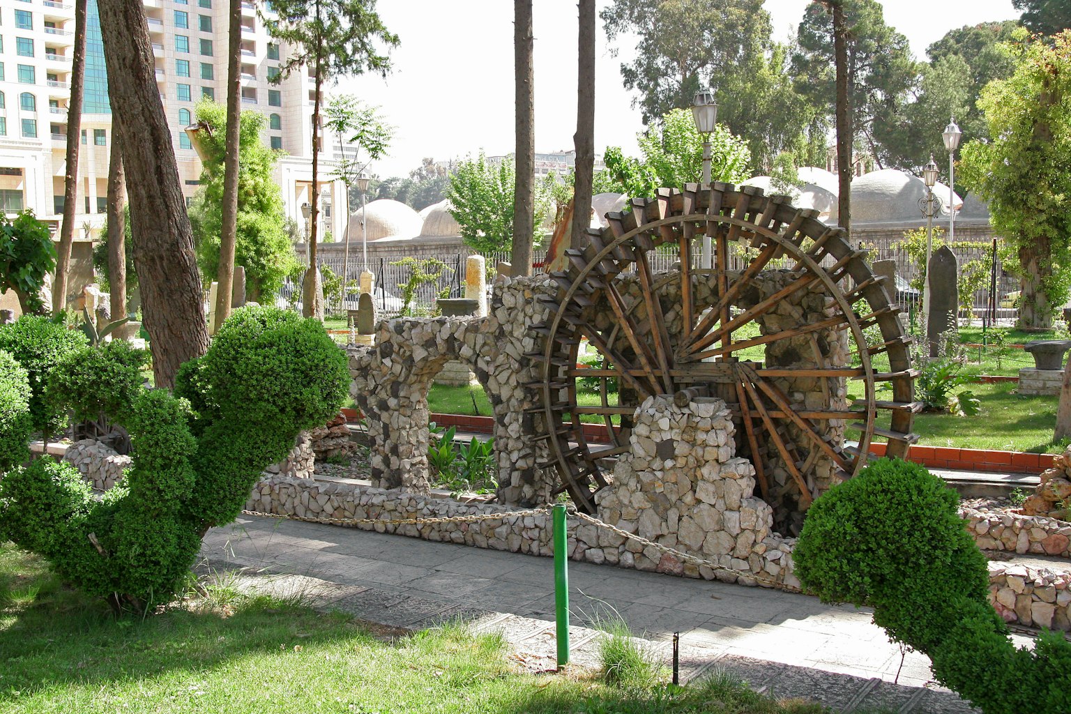Vista escénica de una rueda de agua de madera y una estructura de piedra en un parque verde