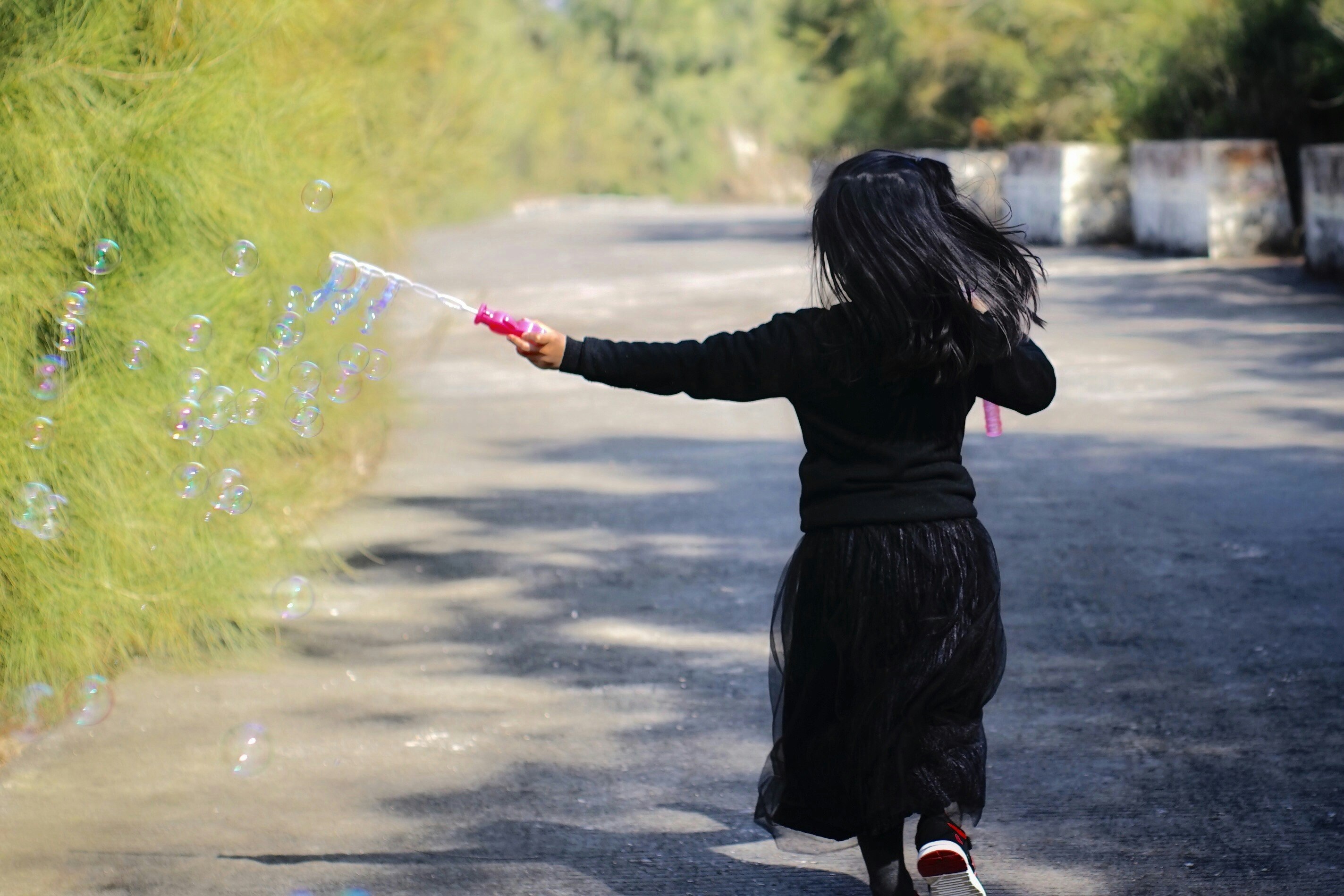 草むらの水しぶきを浴びる黒いコートの子ども