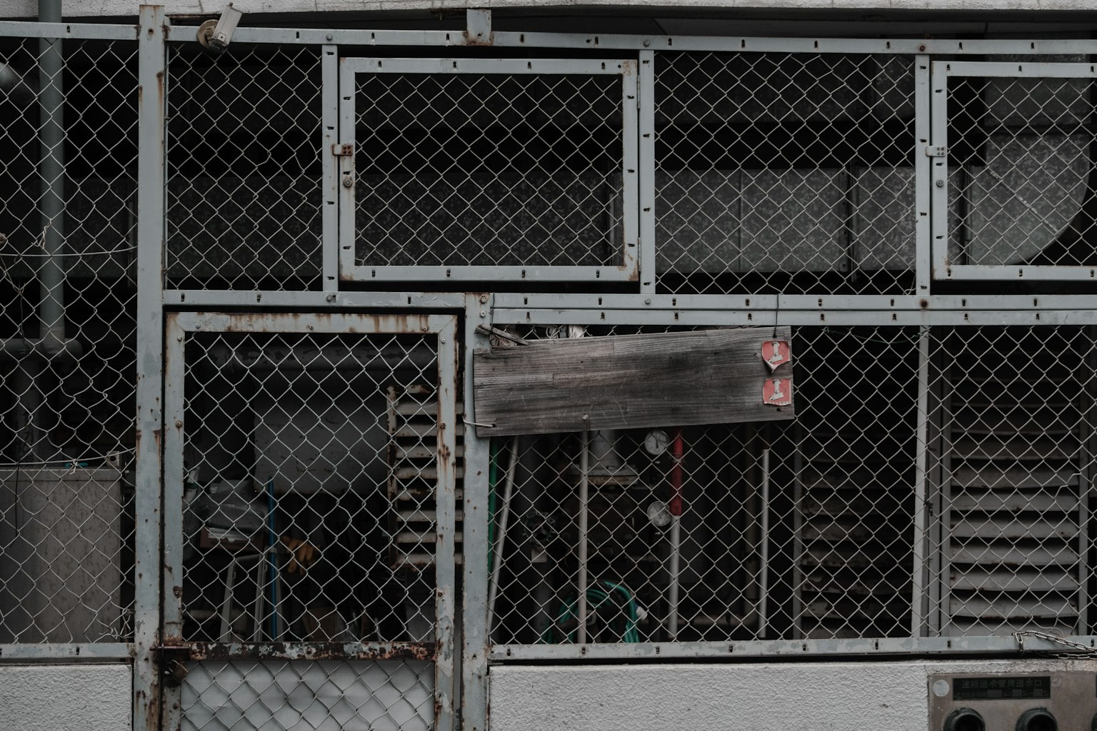 Exterior view of a structure surrounded by metal fencing featuring windows and a door