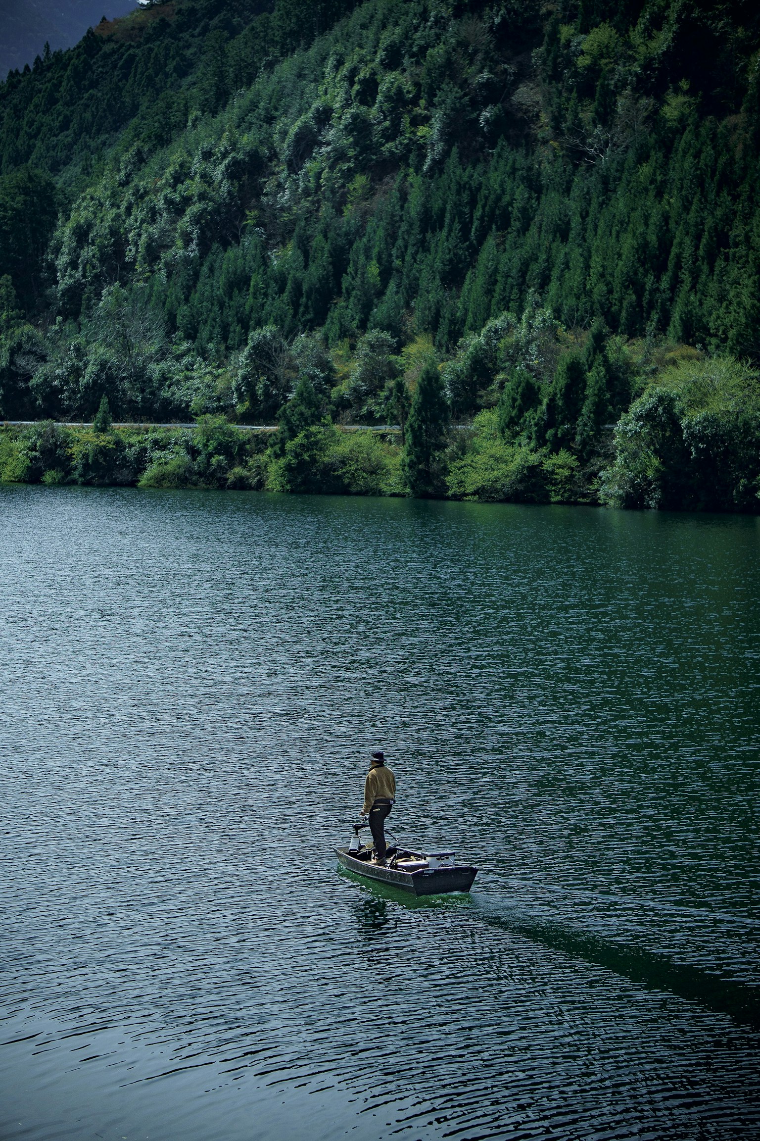 Personne debout dans une petite barque sur un lac entouré de montagnes verdoyantes