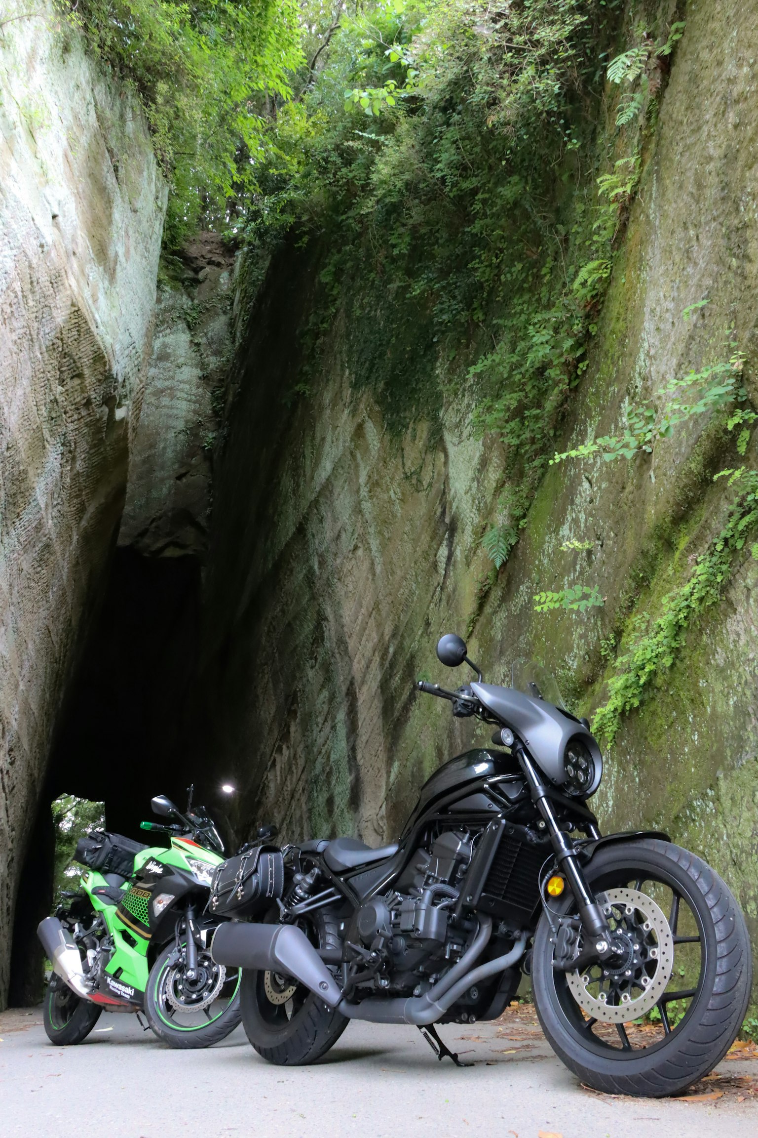 Two motorcycles parked between moss-covered rocks in a narrow passage