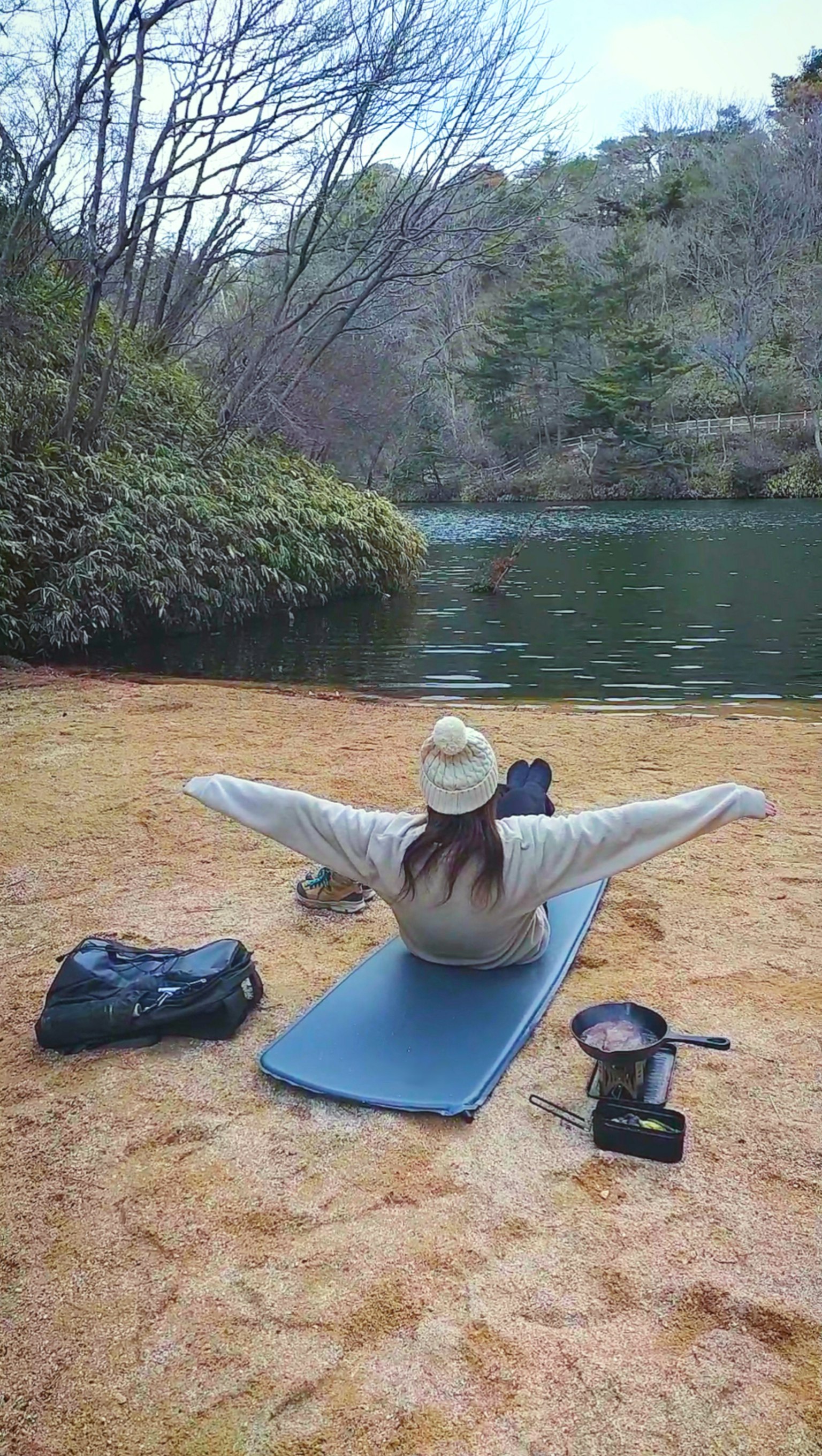 Femme assise sur un tapis de yoga au bord d'un lac, bras écartés